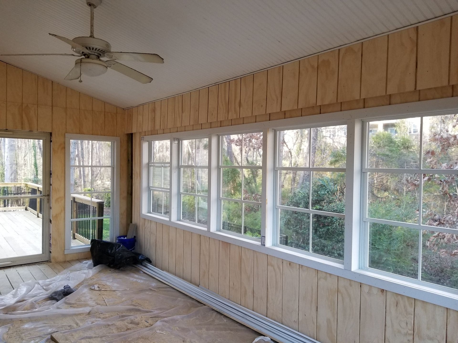 Sunroom with unfinished wood walls, multiple white-framed windows, ceiling fan, and door to a deck.