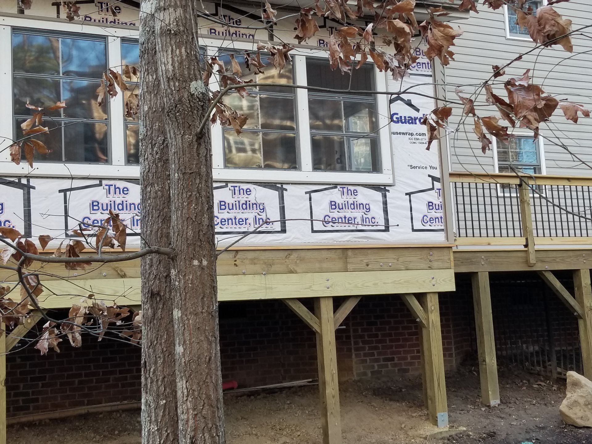 Deck construction with a partially finished building and a tree in the foreground.