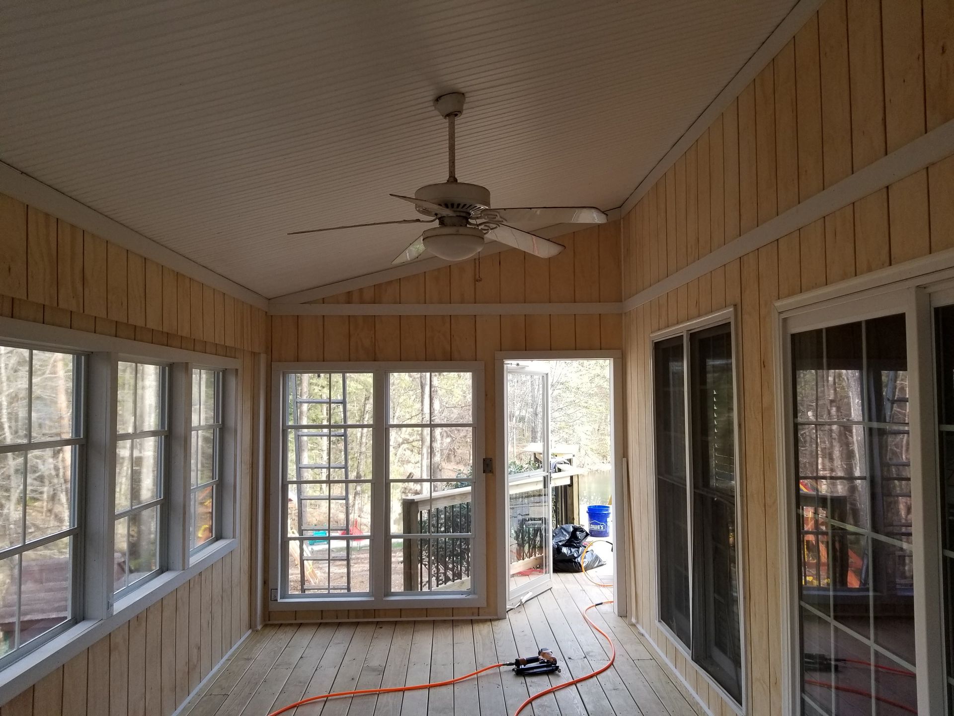 Sunroom with wood paneling, windows, and ceiling fan. Natural light fills the space.