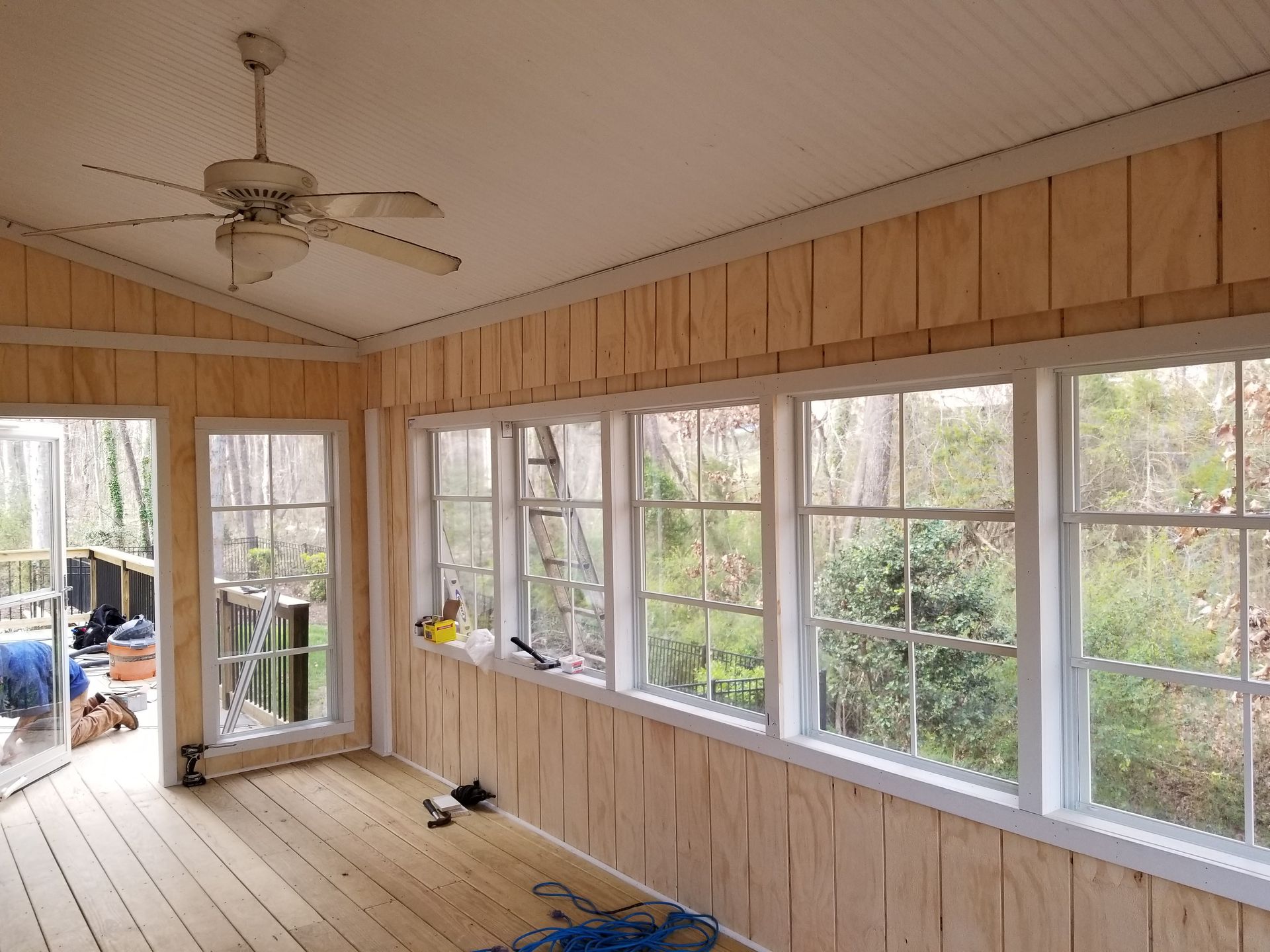 Sunroom interior with windows, wood paneling, and ceiling fan. Light wood flooring and trim.