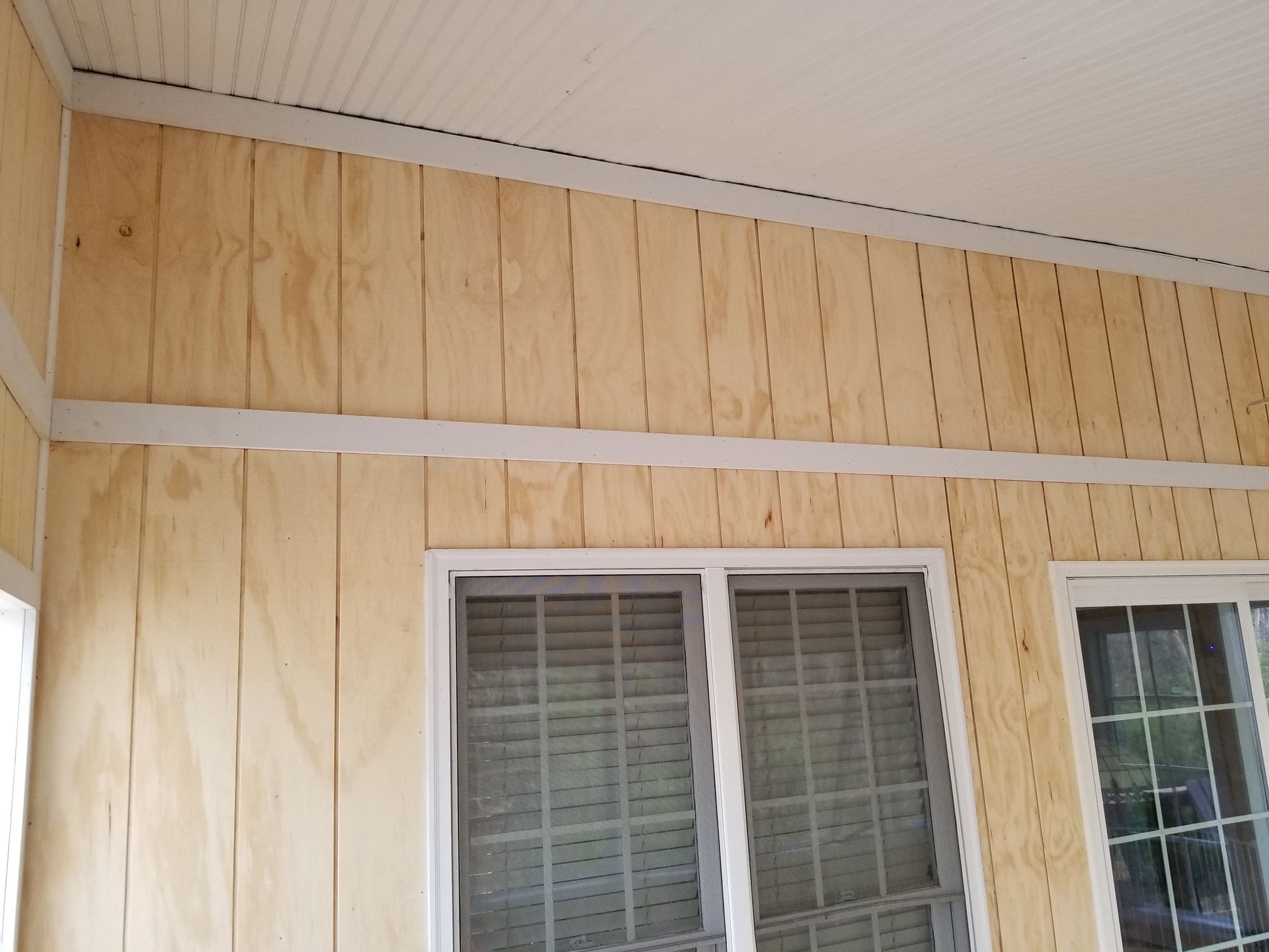 Interior porch with plywood walls and white trim, windows visible.