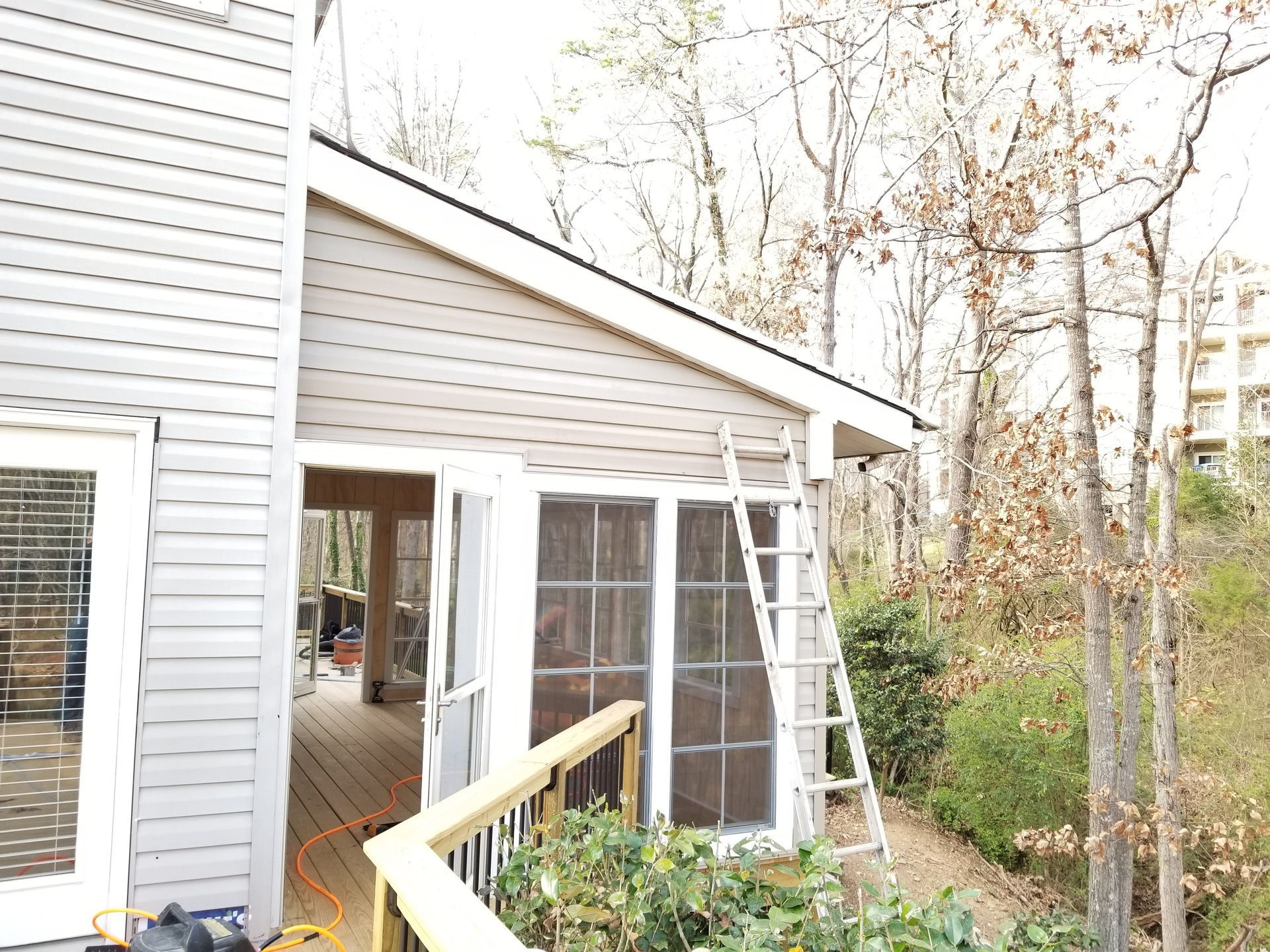 A screened porch with a ladder leaning against it, deck, and trees in the background.