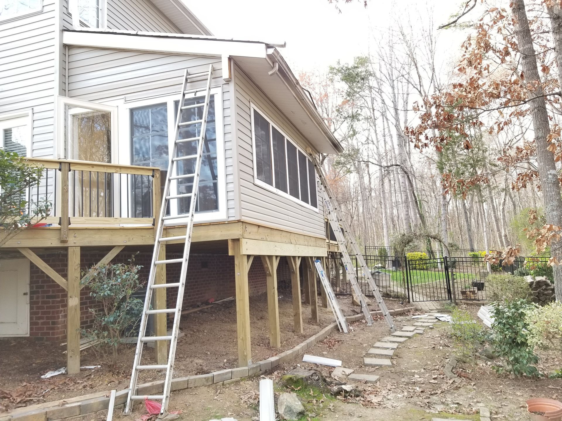 A house with a deck and enclosed porch. Ladders are leaning against the house; a stone path leads to the backyard.