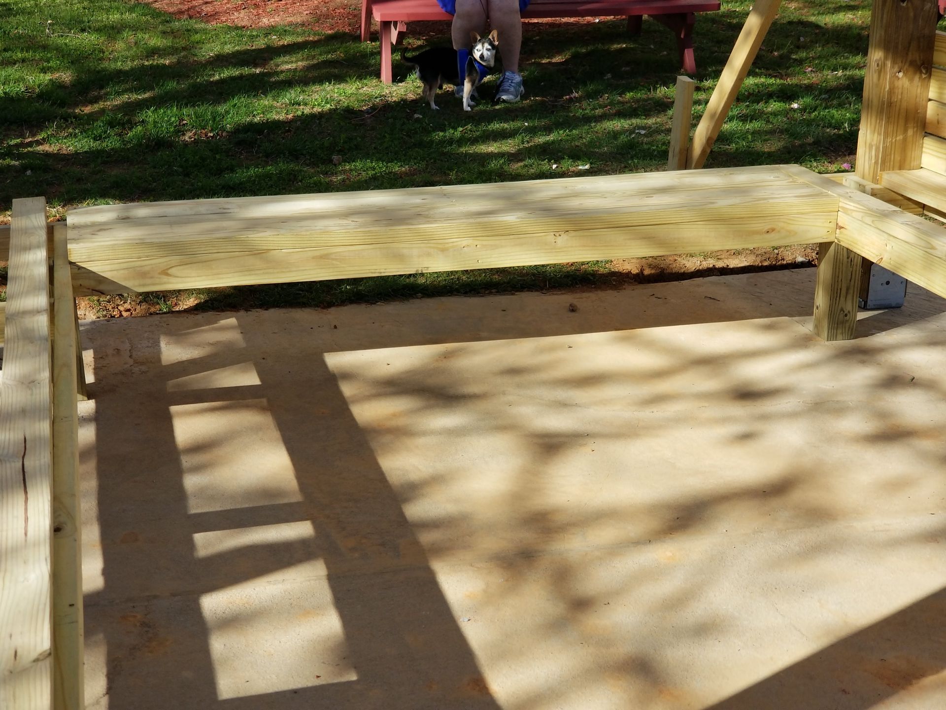 Wooden deck construction; child sitting on a red bench in the background. Sunny outdoor setting.