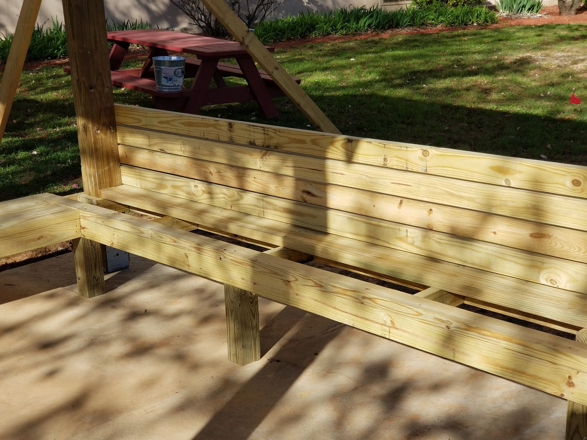 Wooden swing bench under a wooden structure in a yard.