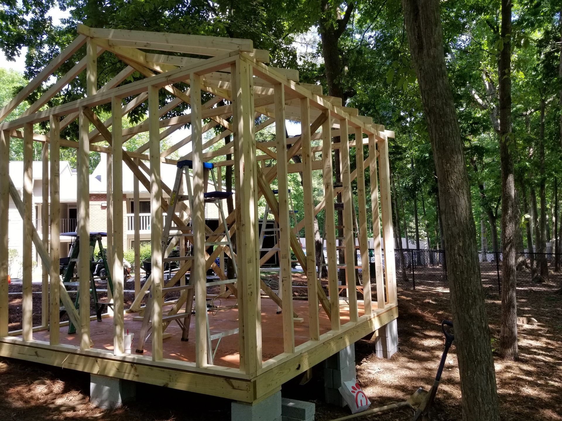 Wooden shed frame under construction outdoors, in a wooded area.