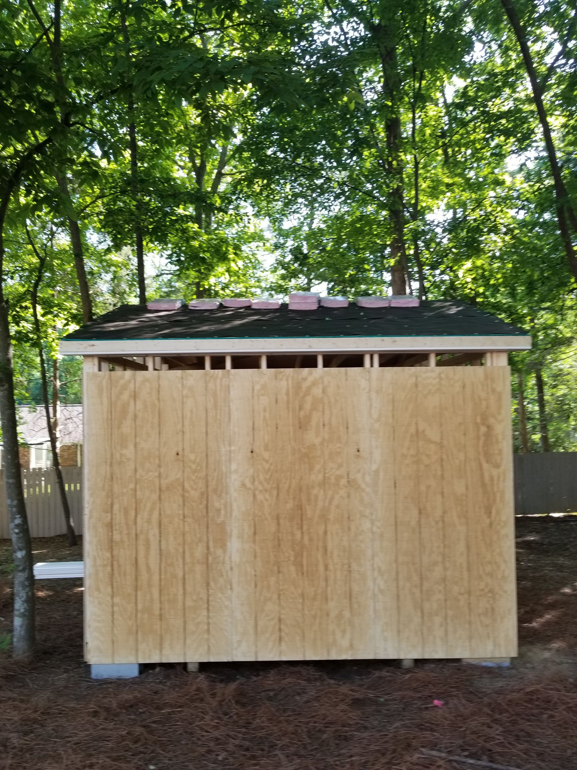 Wooden shed under construction, green roof, set against a backdrop of trees.