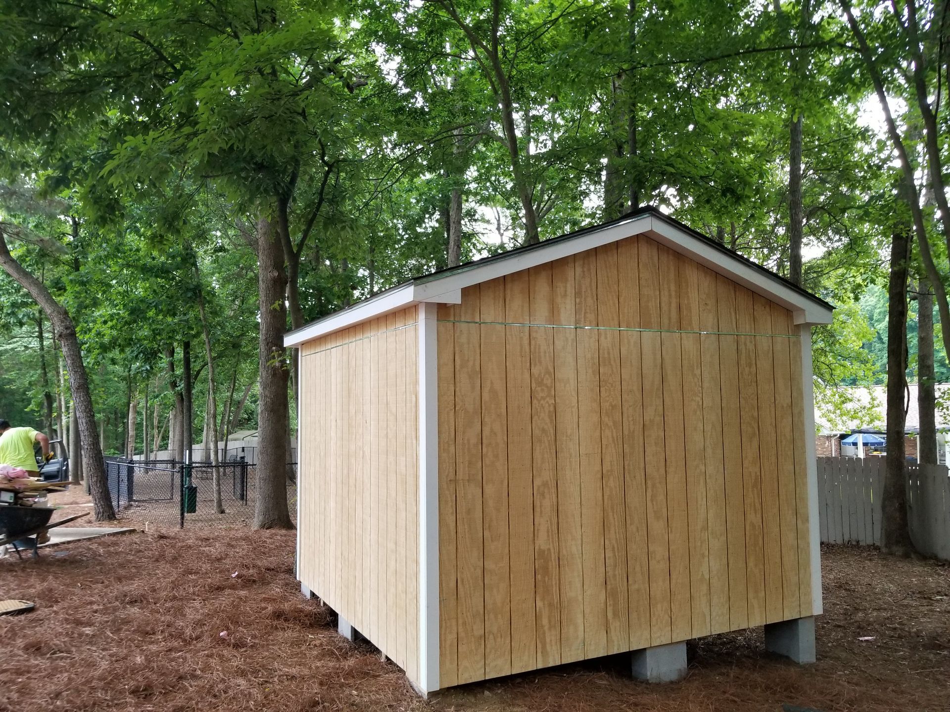 Newly built wooden shed with white trim, sitting on concrete blocks, surrounded by trees.