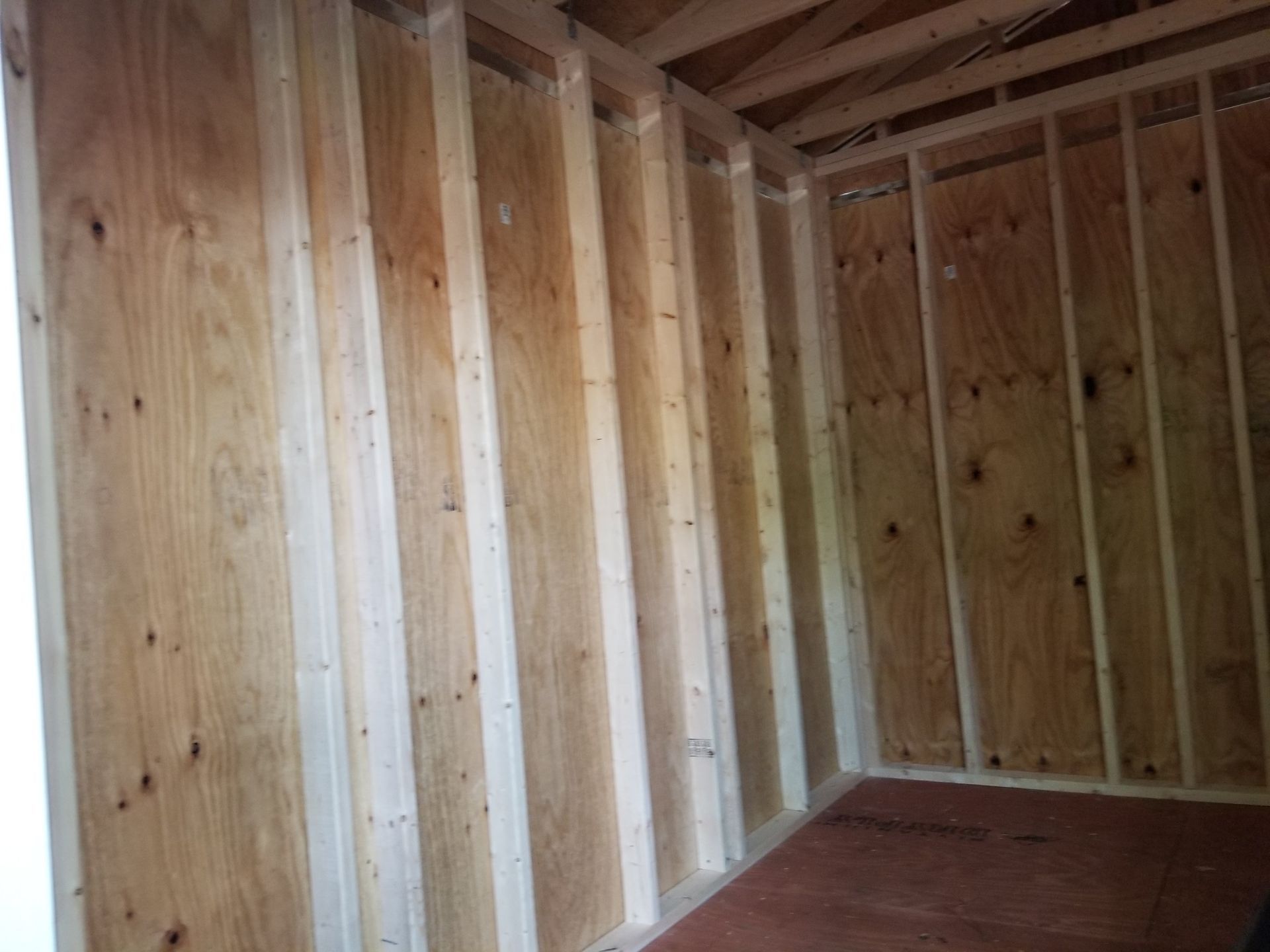Interior view of a wooden shed under construction with plywood walls and floor.