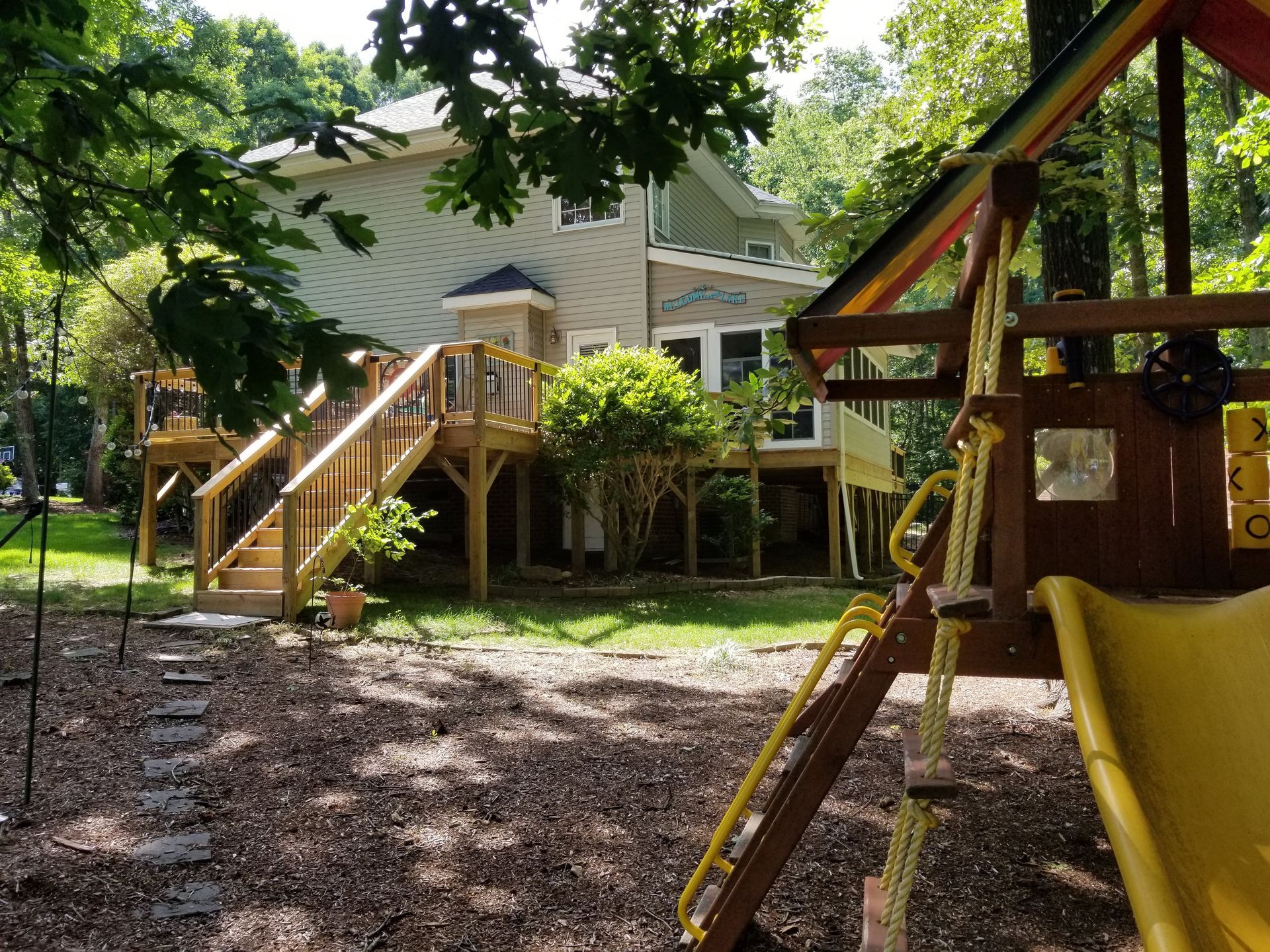 Backyard with a raised deck, wooden playset, and a two-story house with light siding and dark roof.