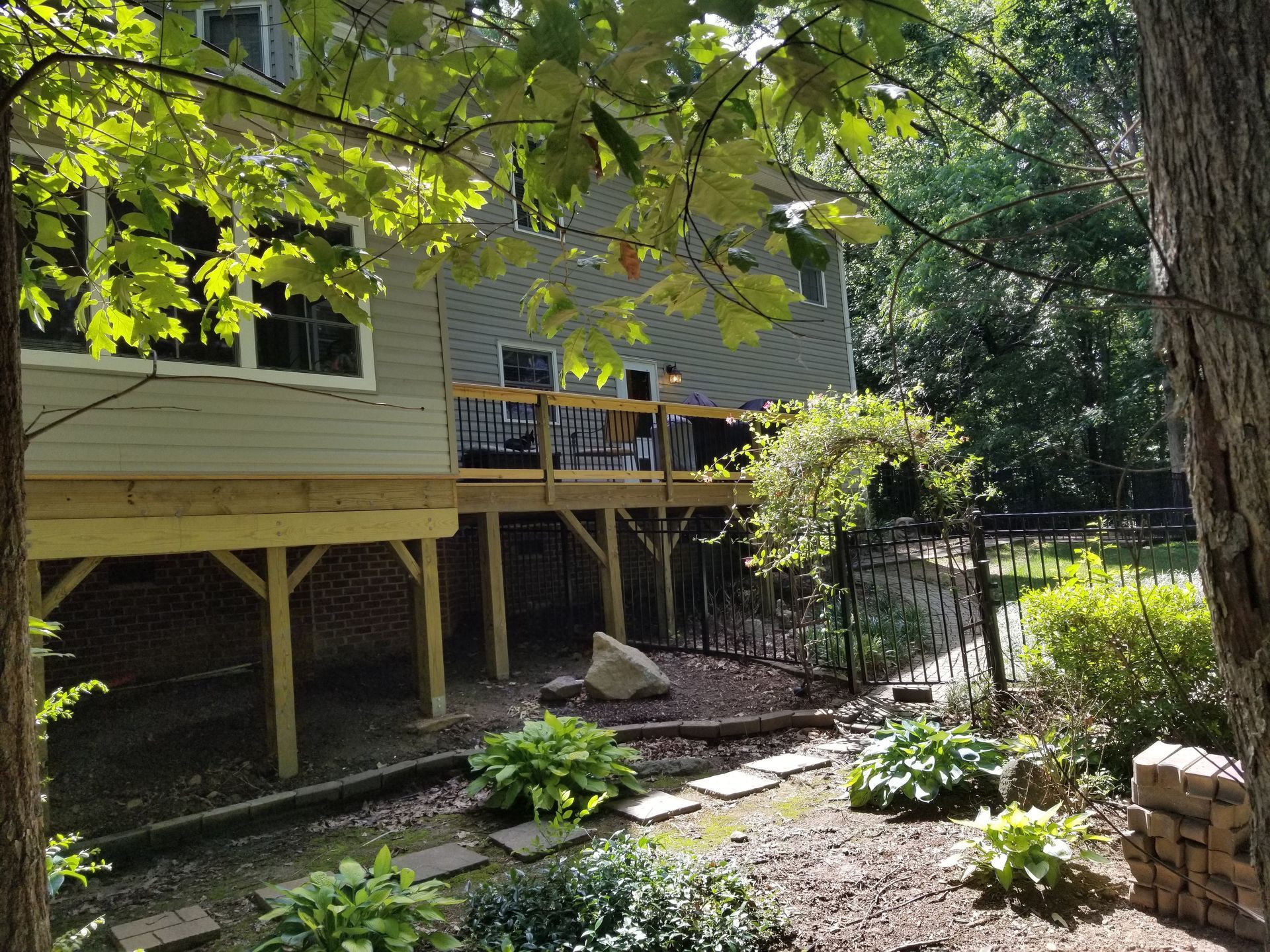 Wooden deck extends from a two-story house, overlooking a landscaped yard.