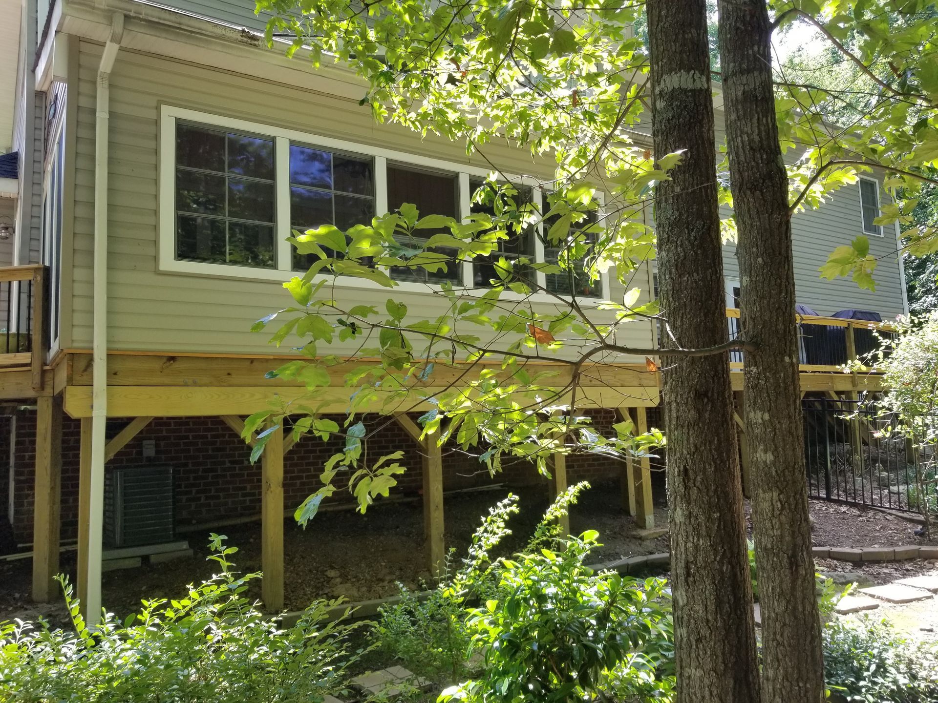 Deck attached to a two-story house with a sunroom, seen from a wooded yard.