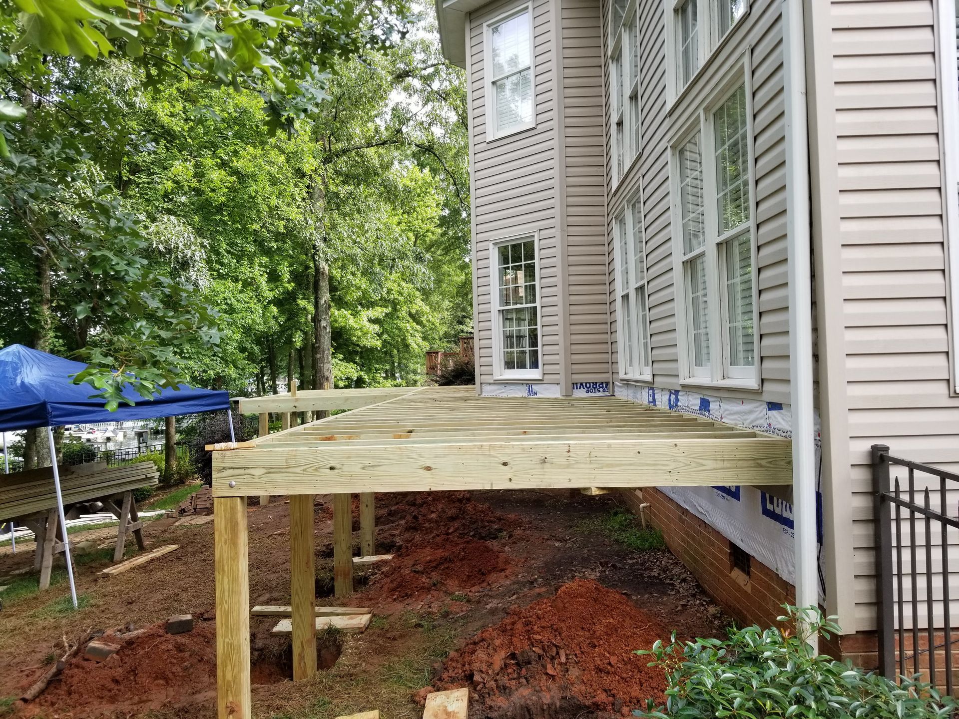 New wooden deck under construction next to a beige house, over dirt.