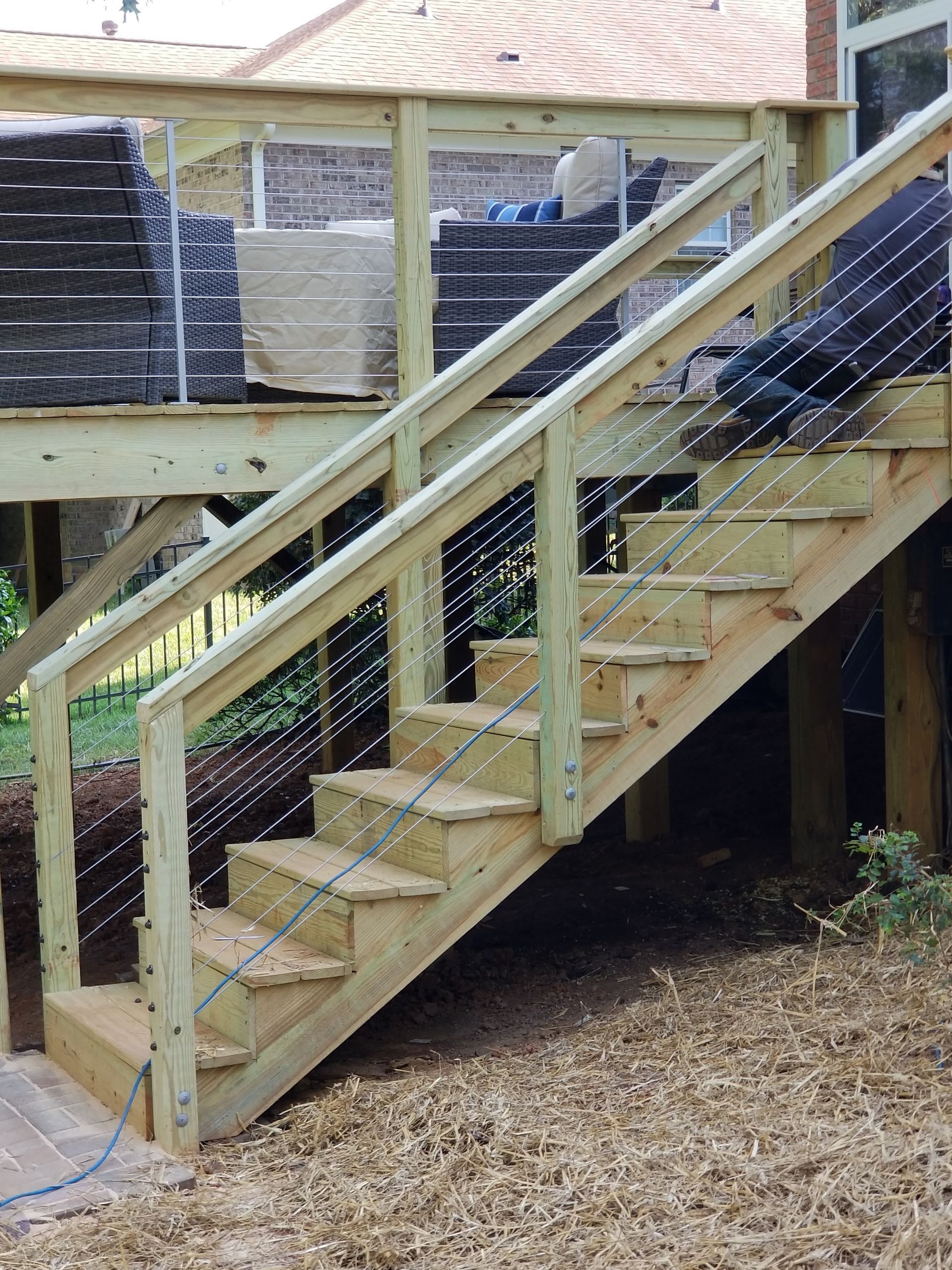 Wooden outdoor staircase with cable railing, leading down from a deck.