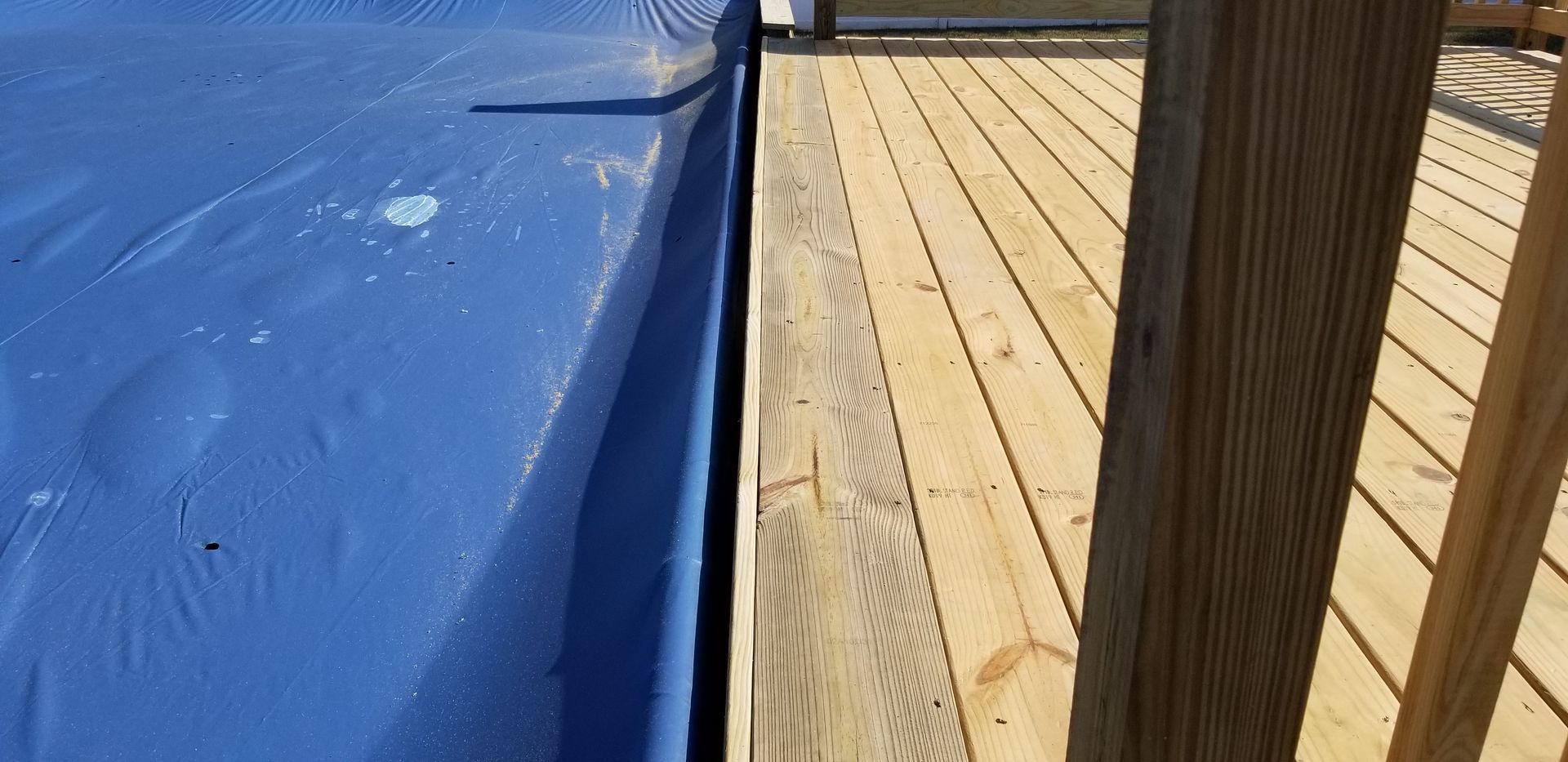 Blue tarp next to a wooden deck with railing.