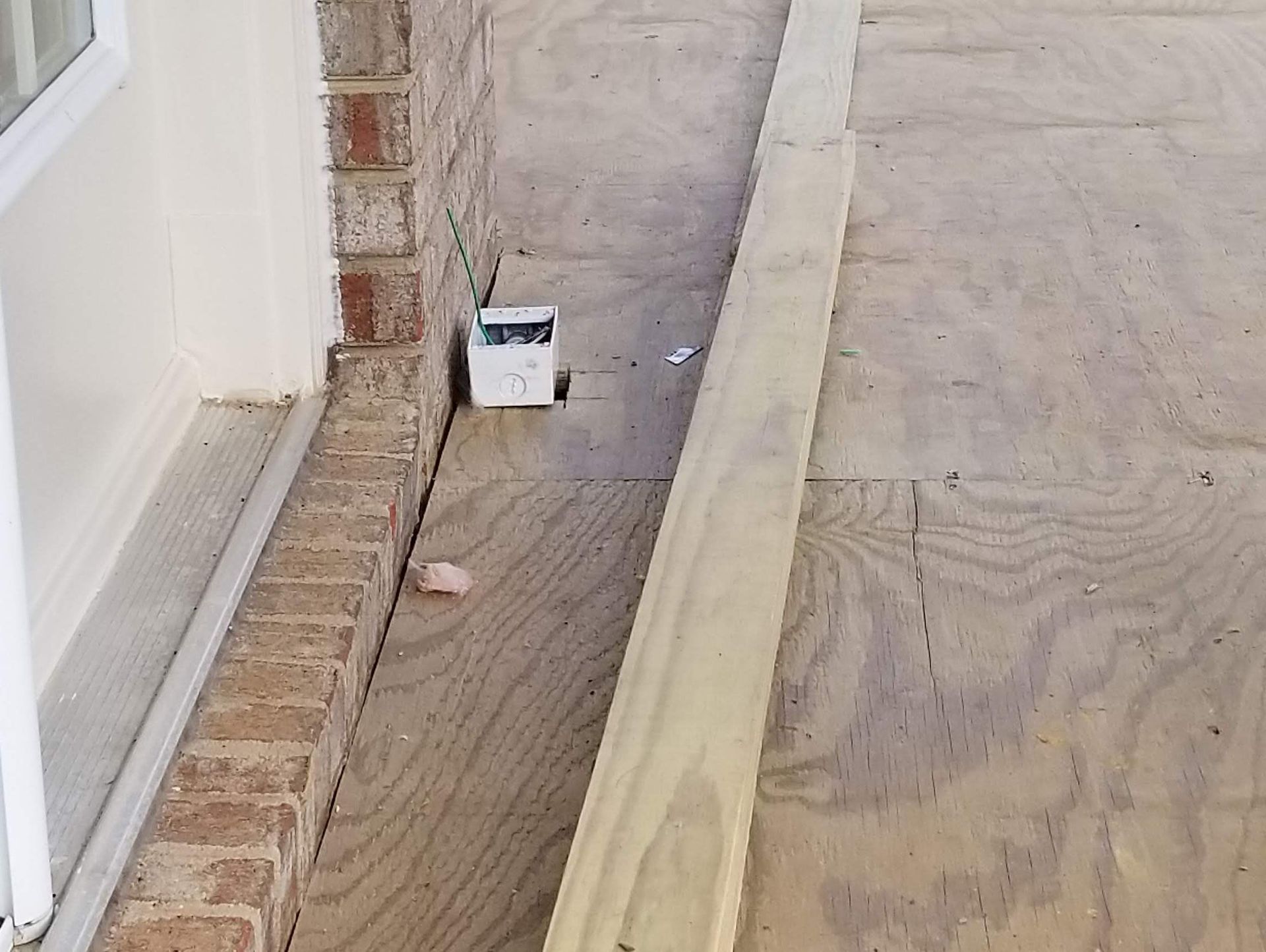 Ramp built from plywood and lumber next to a brick wall and door, with a white electrical box visible.