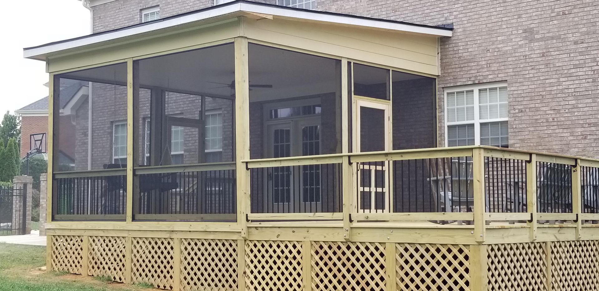 Screened-in porch and deck attached to a brick house. Beige wood construction with black screens and railings.