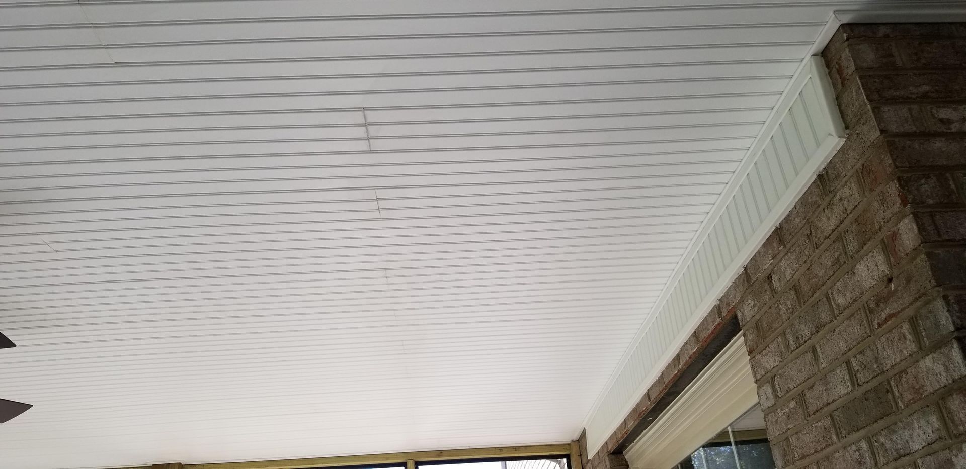 White patterned ceiling with trim against a brick wall.