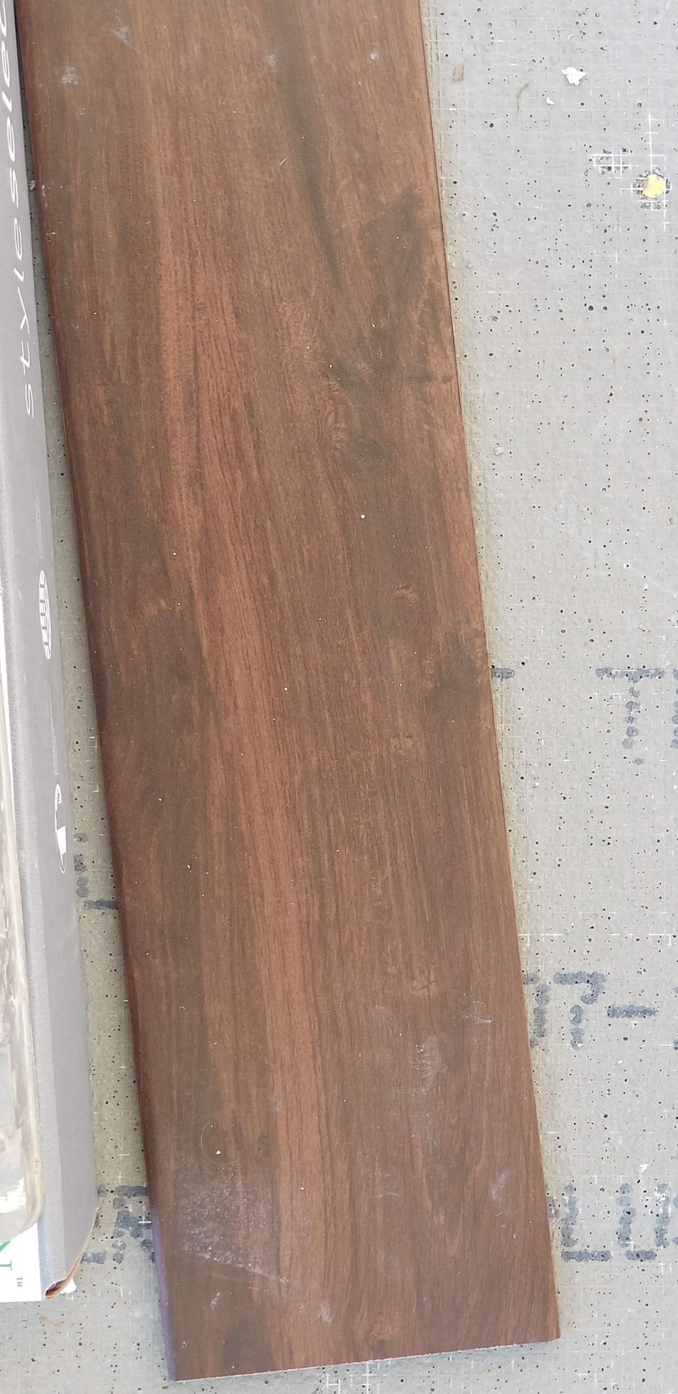A close-up of a wooden plank with a dark brown color and visible wood grain on a light surface.