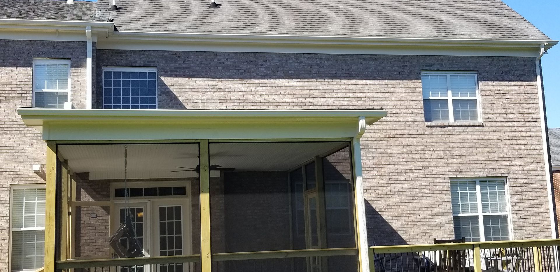 Back of a house with a screened porch and multiple windows; neutral tones and natural light.