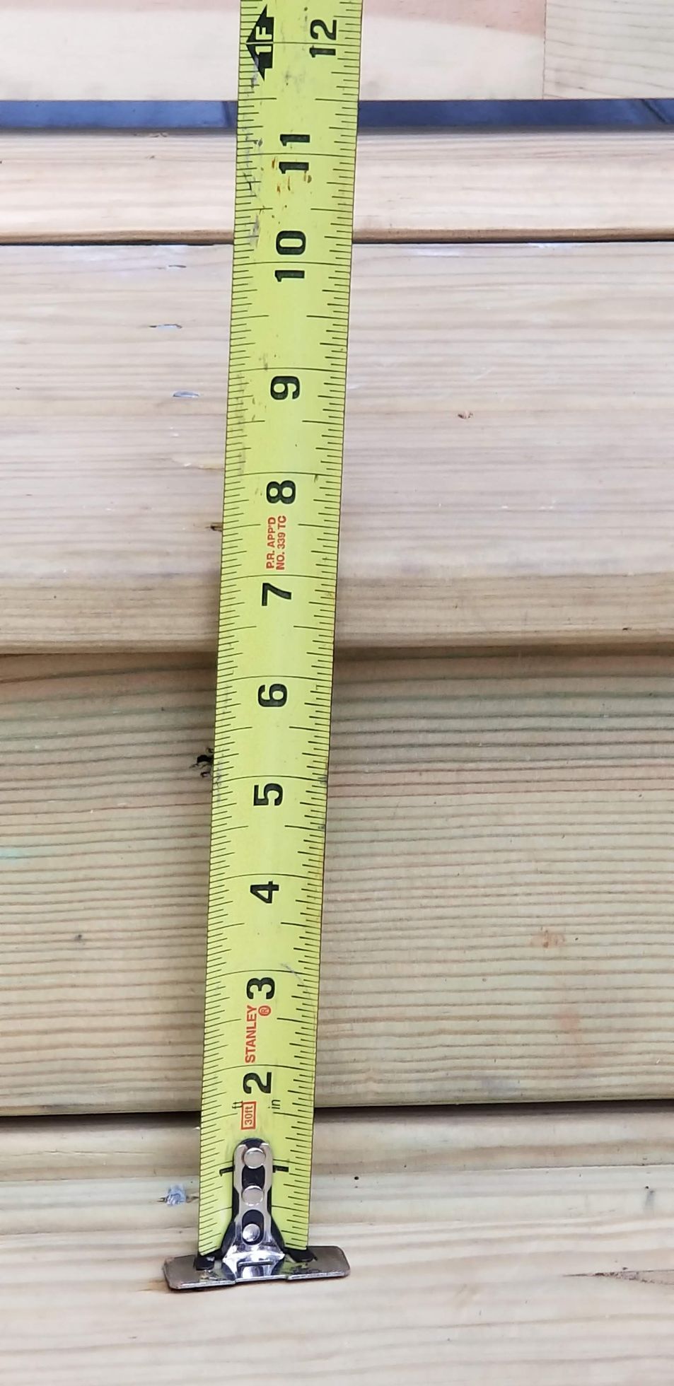 Yellow tape measure against light-colored wooden planks.