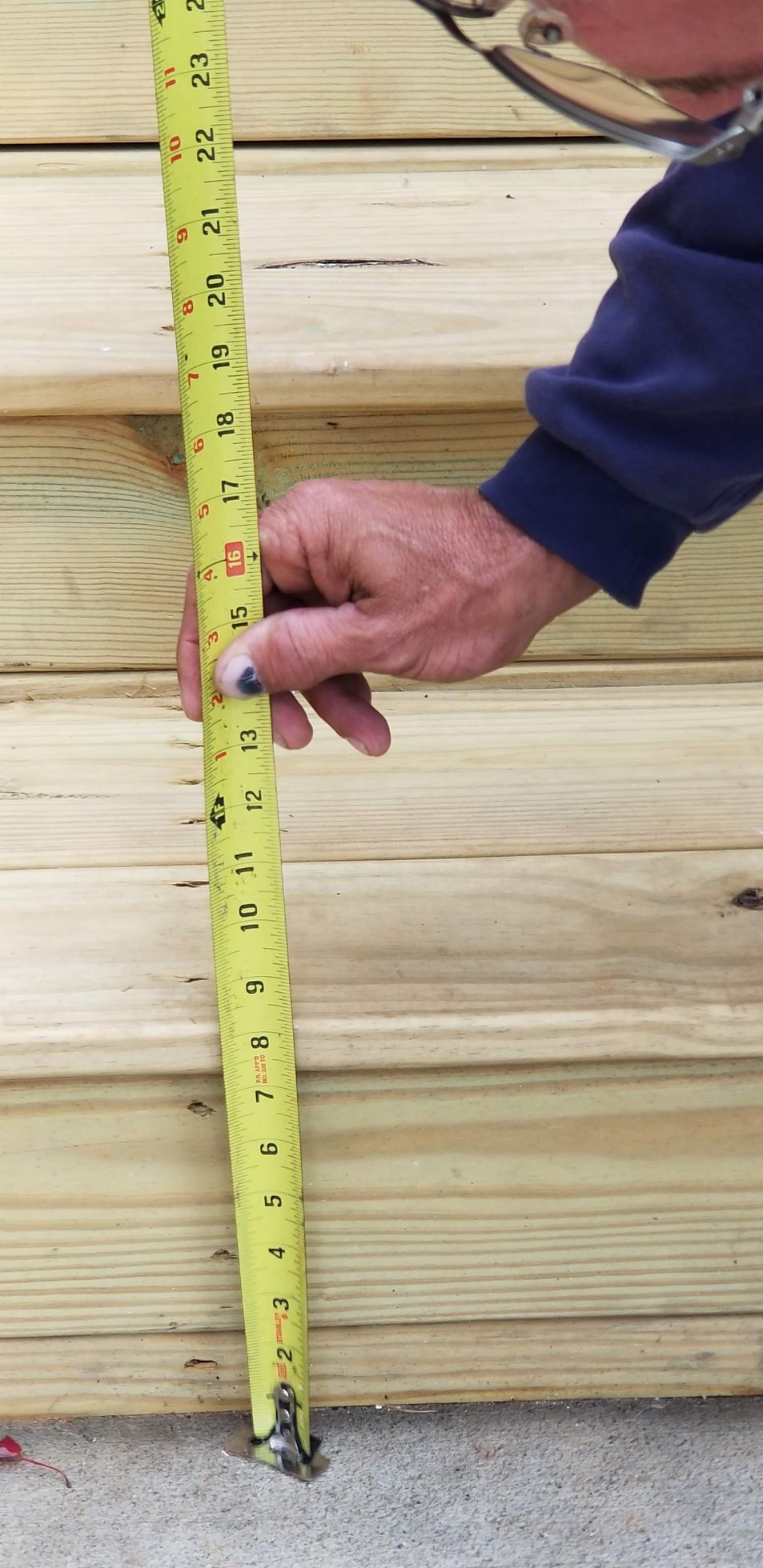 Person measuring wooden steps with a yellow tape measure, likely for construction or renovation.