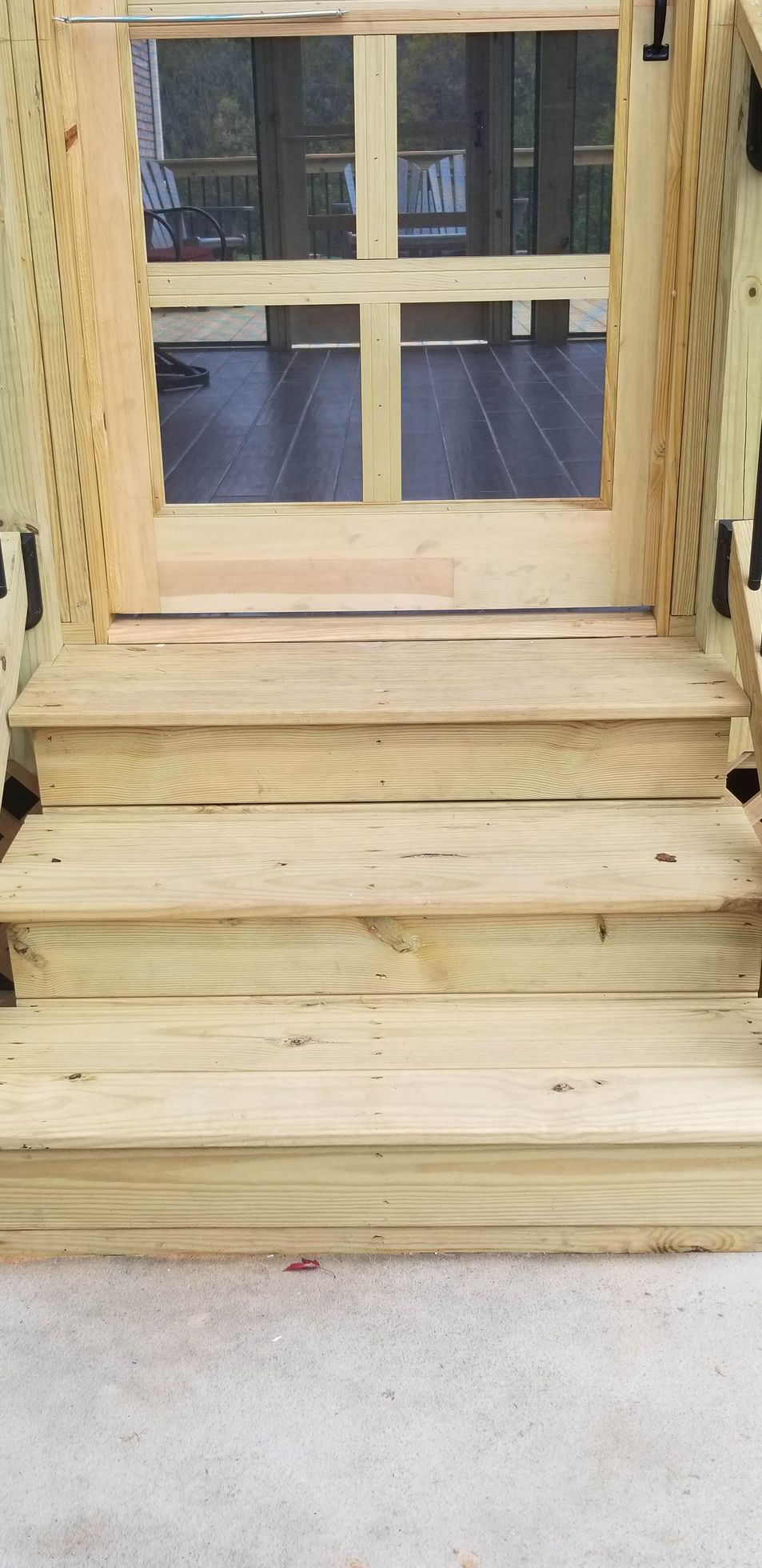 Wooden steps leading up to a screen door, with a glimpse of an outdoor setting through the glass.