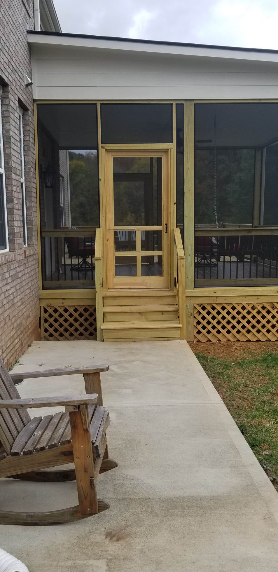 Screened porch with steps and door, leading to a concrete walkway. Wooden rocking chair on the left.