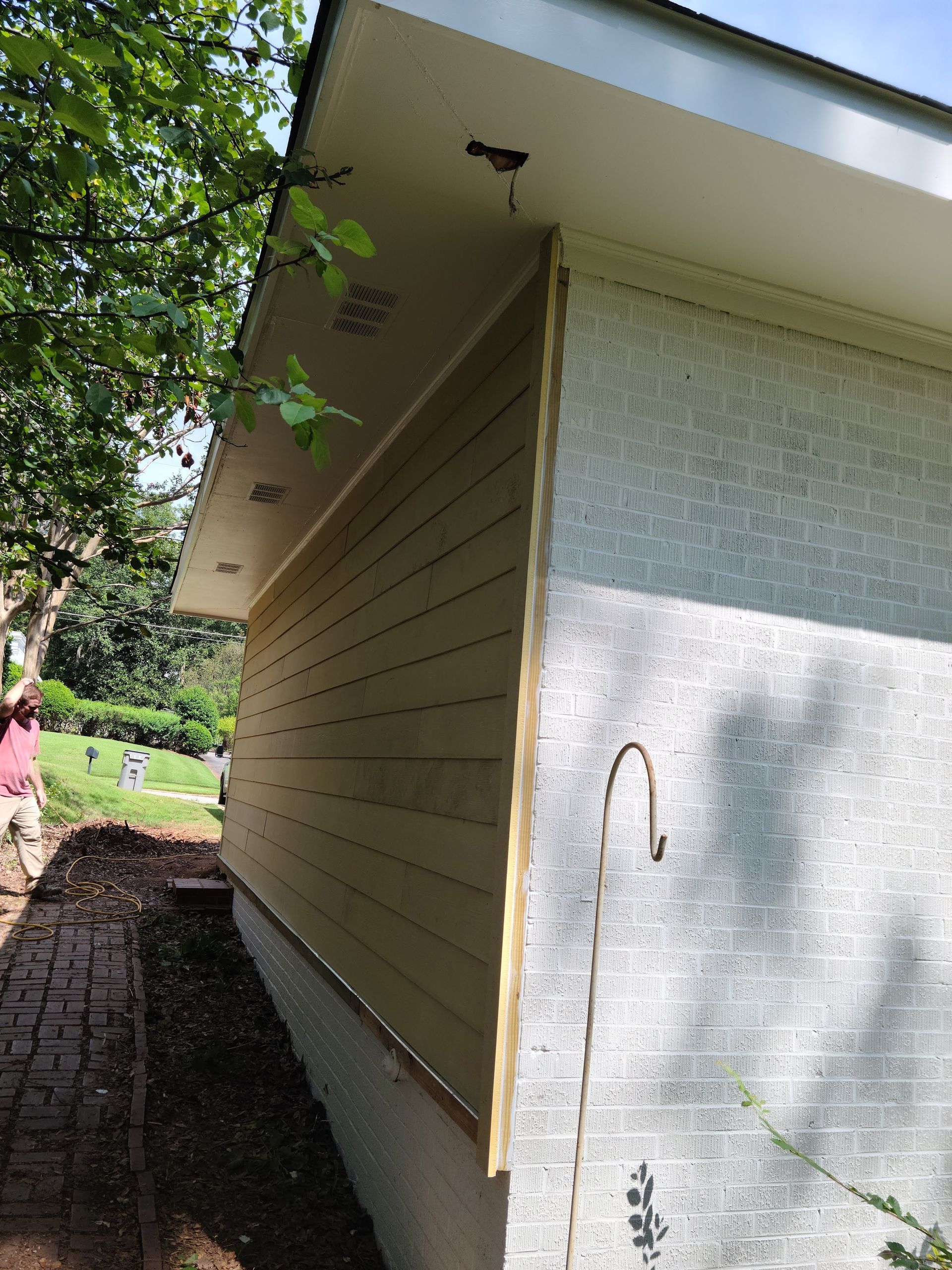 Side view of a building with light yellow siding and a white brick wall.