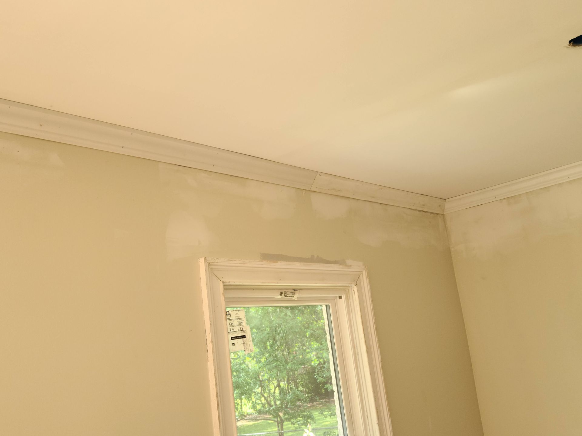 Interior view of a room with a window, crown molding, and painted beige walls; some patches.