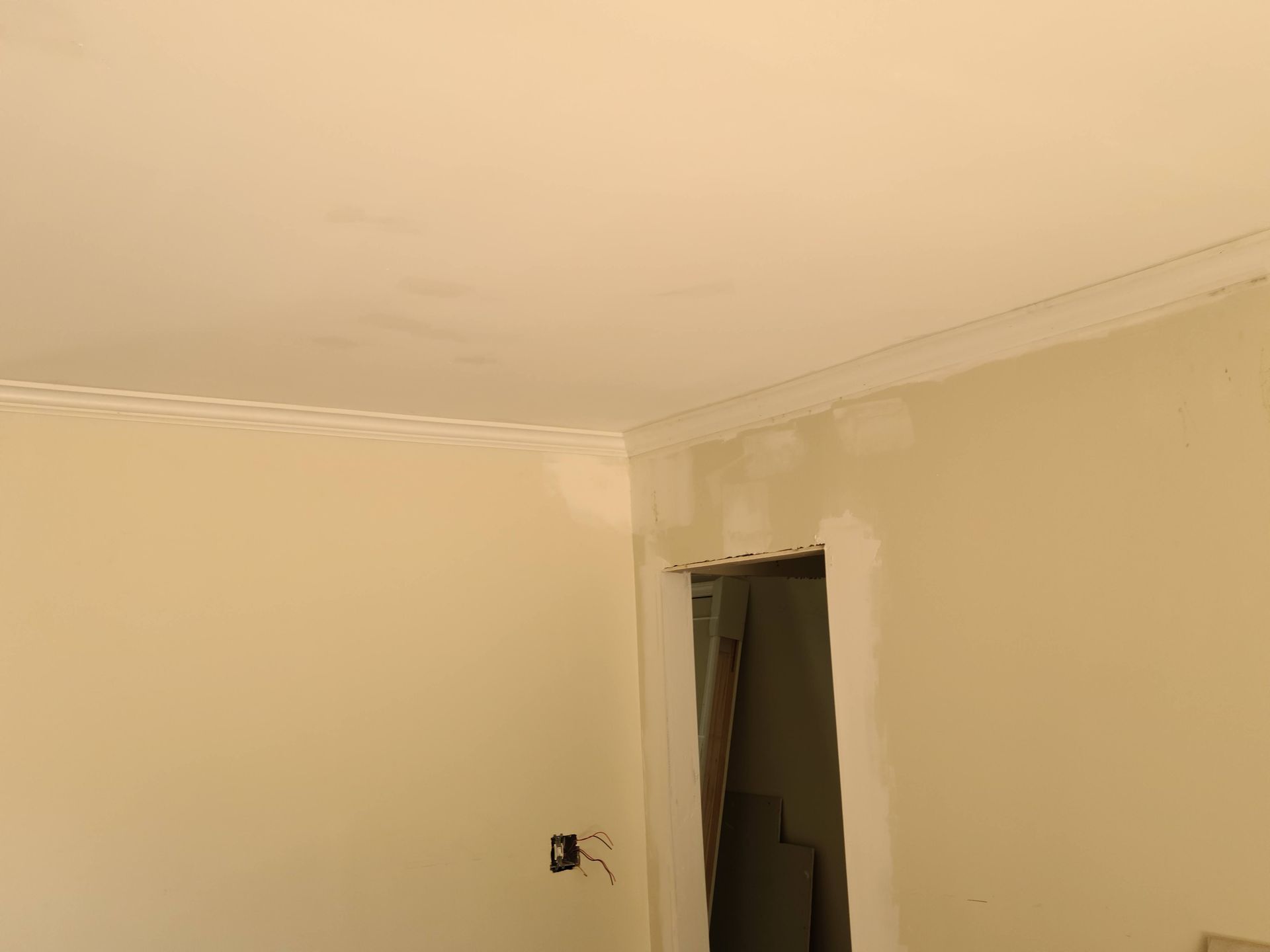 Interior view of a room, walls and ceiling are cream colored, with crown molding. An open doorway is visible.