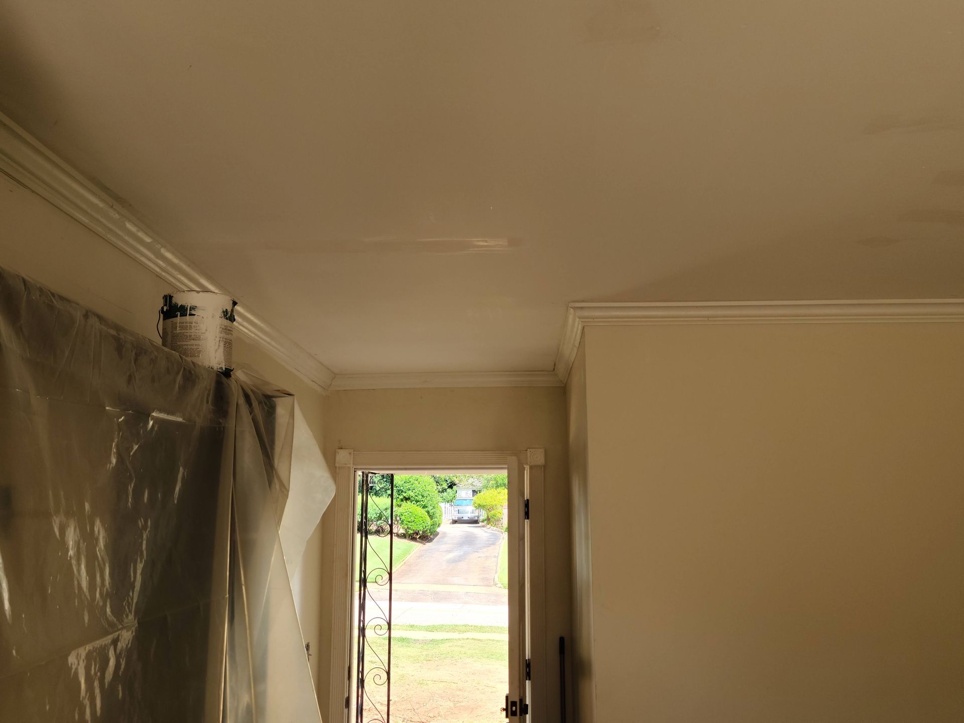 Interior view of a room with an open doorway leading outside. Ceiling and walls are light-colored. Plastic sheet is hanging on the left.
