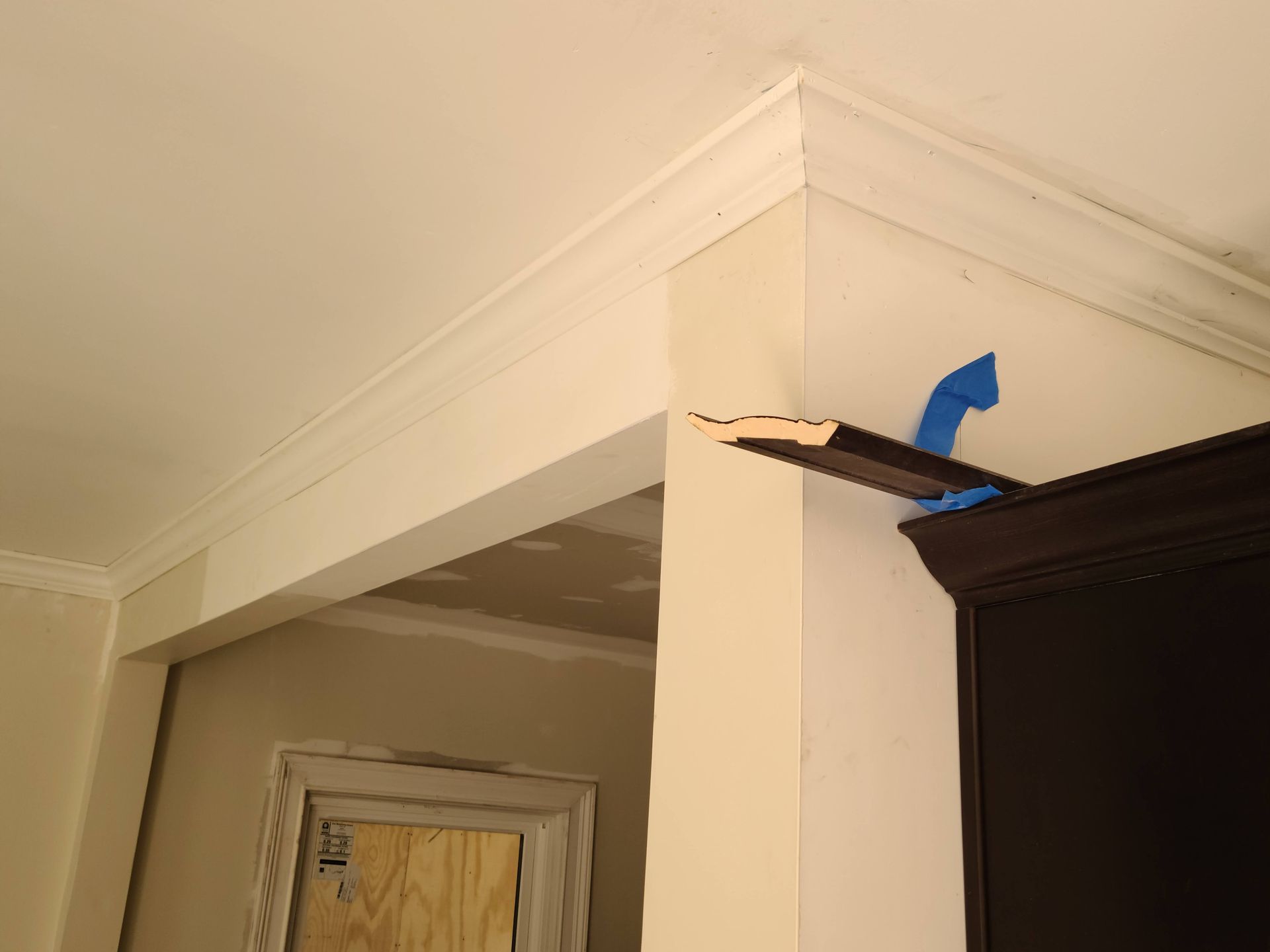 Corner of a room with white crown molding. A piece of crown molding is supported by a blue tool.