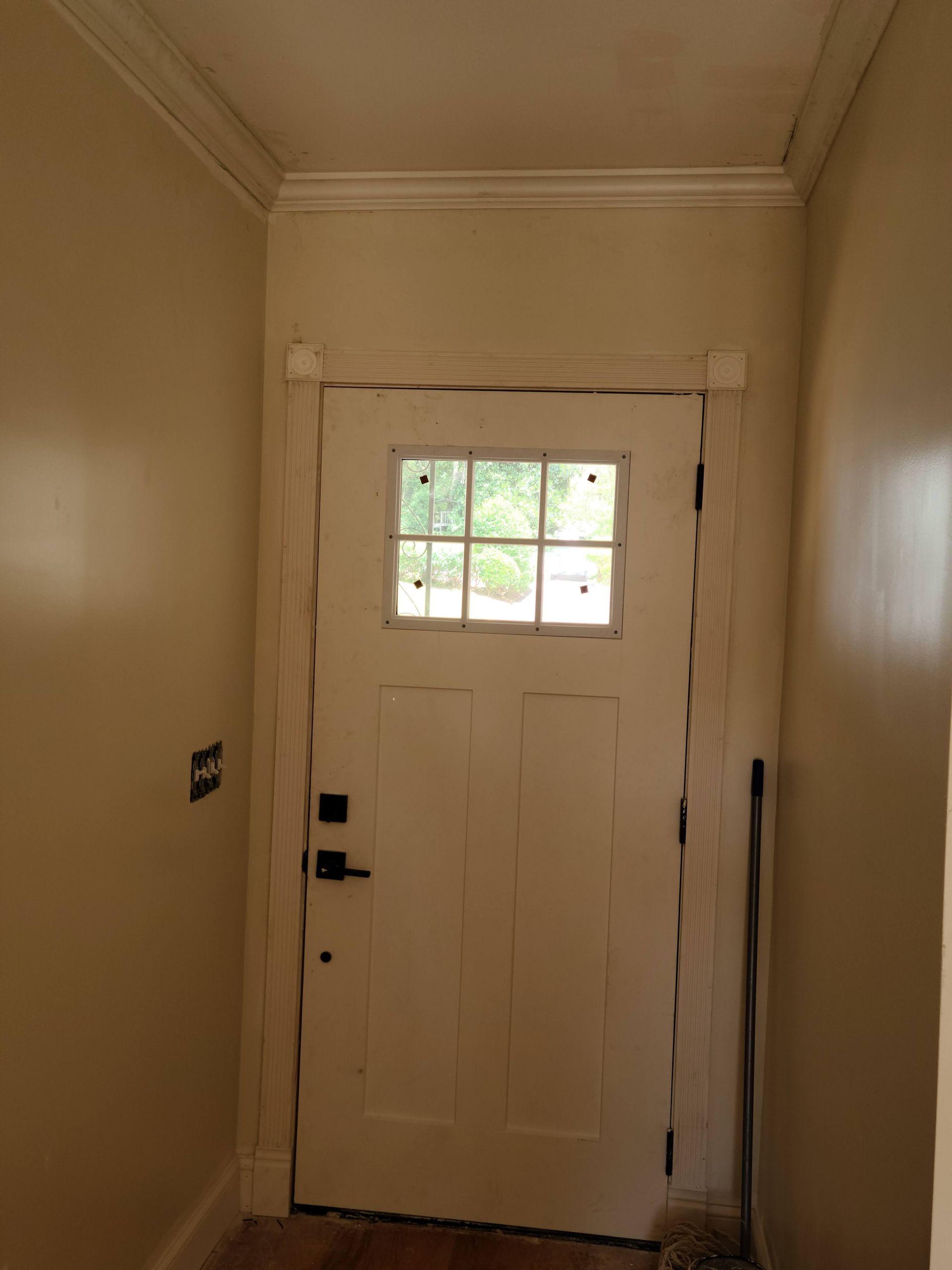White door with window, surrounded by tan walls and molding, black handle and lock.