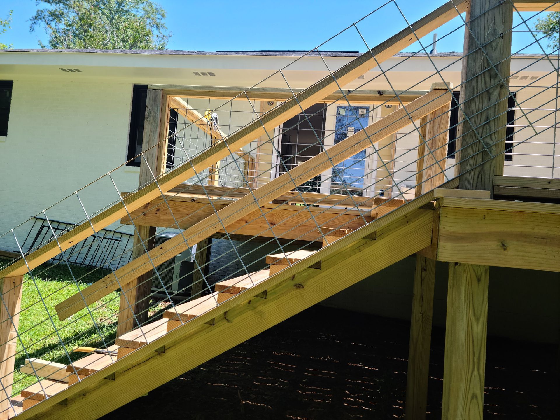 Wooden deck with staircase and cable railing leading to a house.