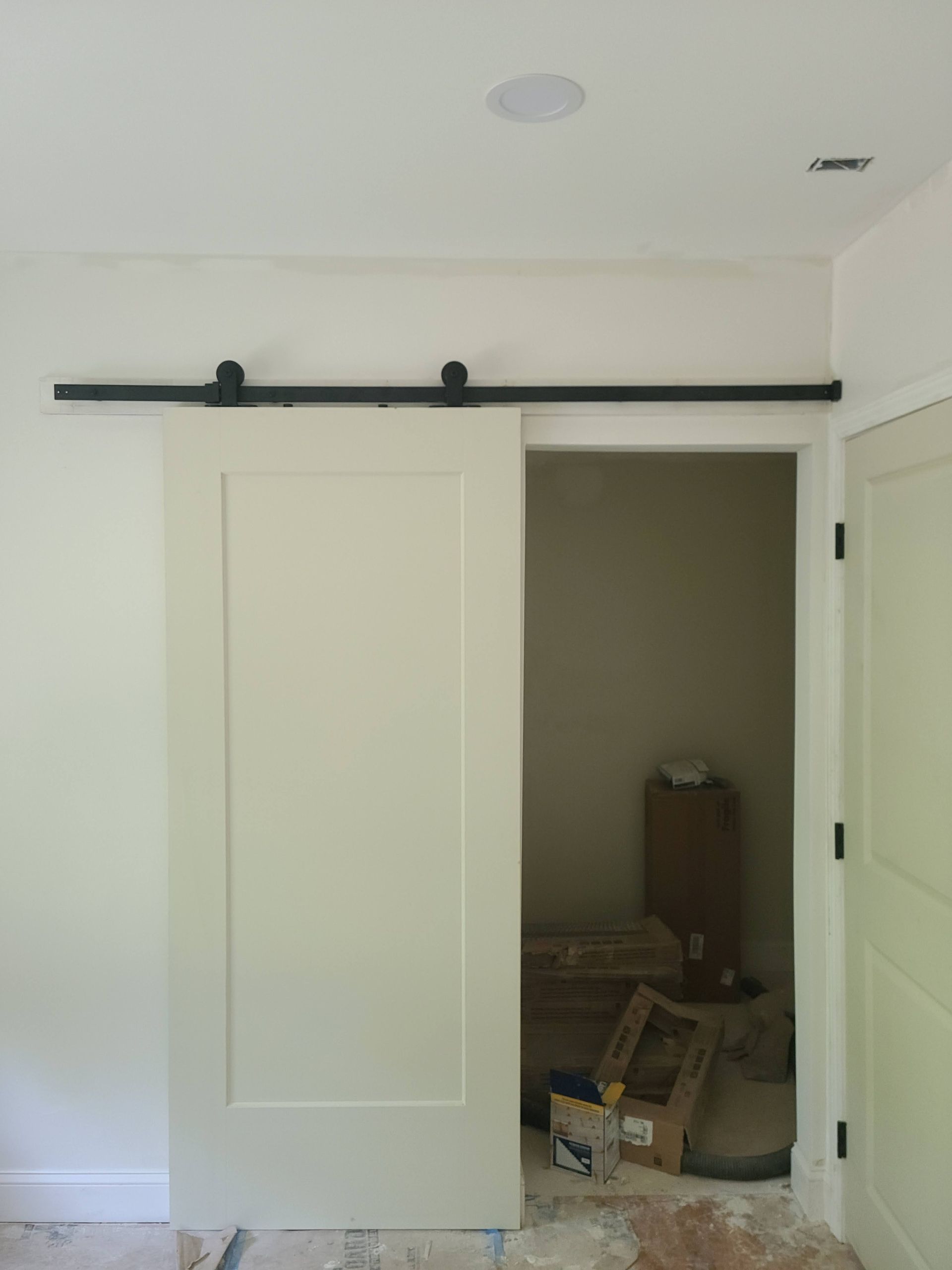 White sliding barn door, black track, partially open, revealing a room with construction materials.