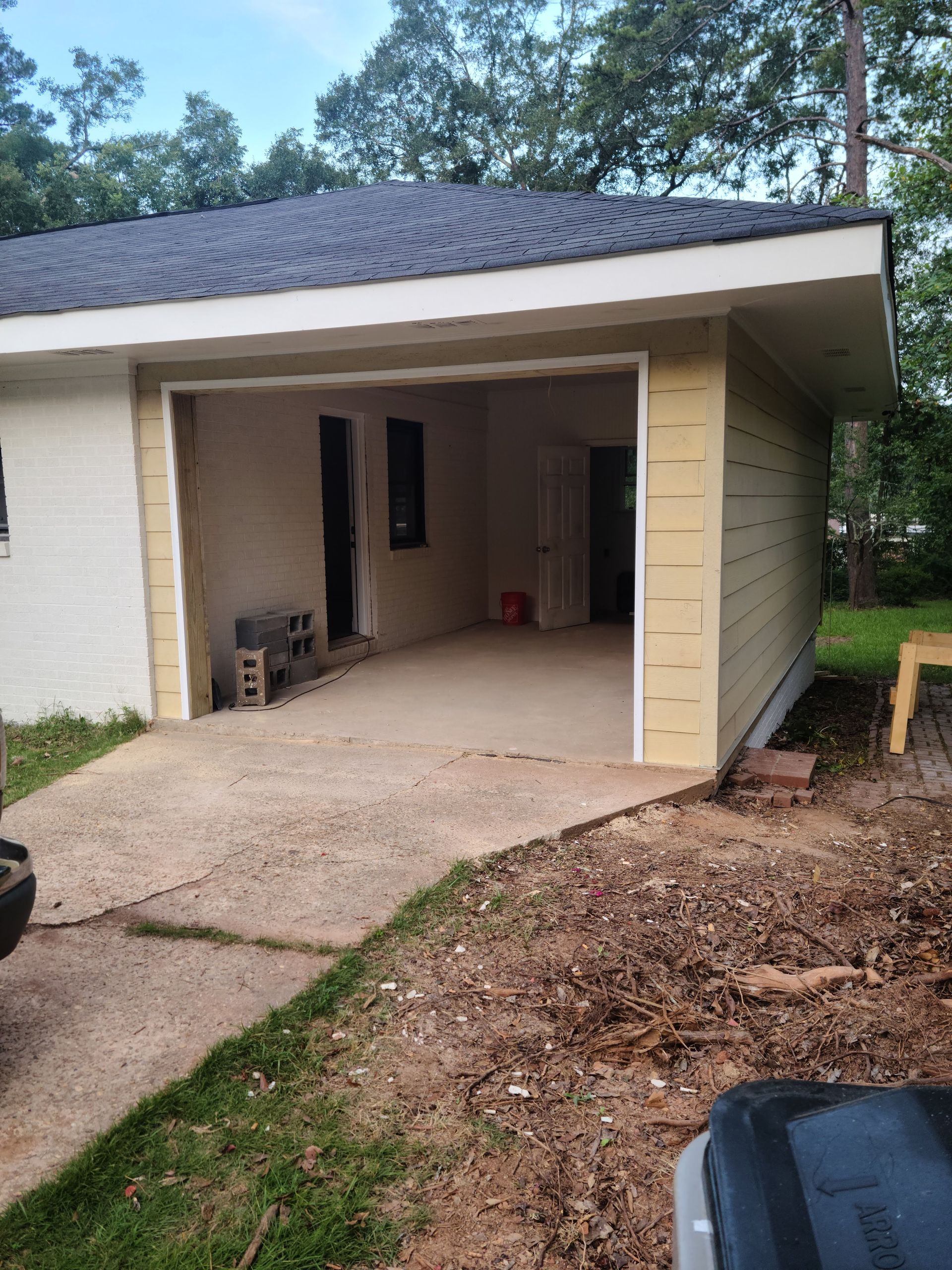 Garage with an open entrance, concrete driveway, and tan siding.