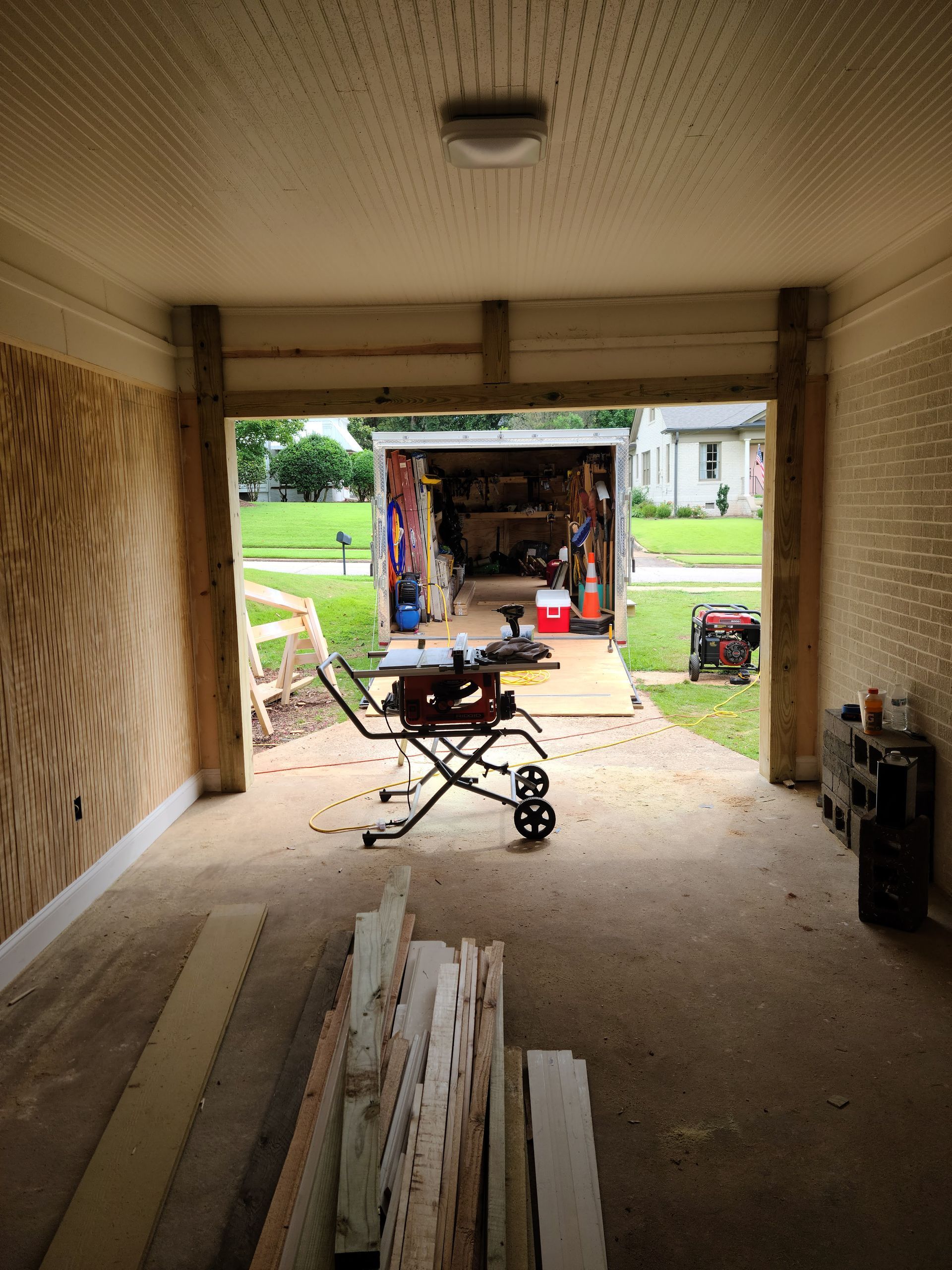Garage interior with wood trim, tools, and a trailer in the opening.