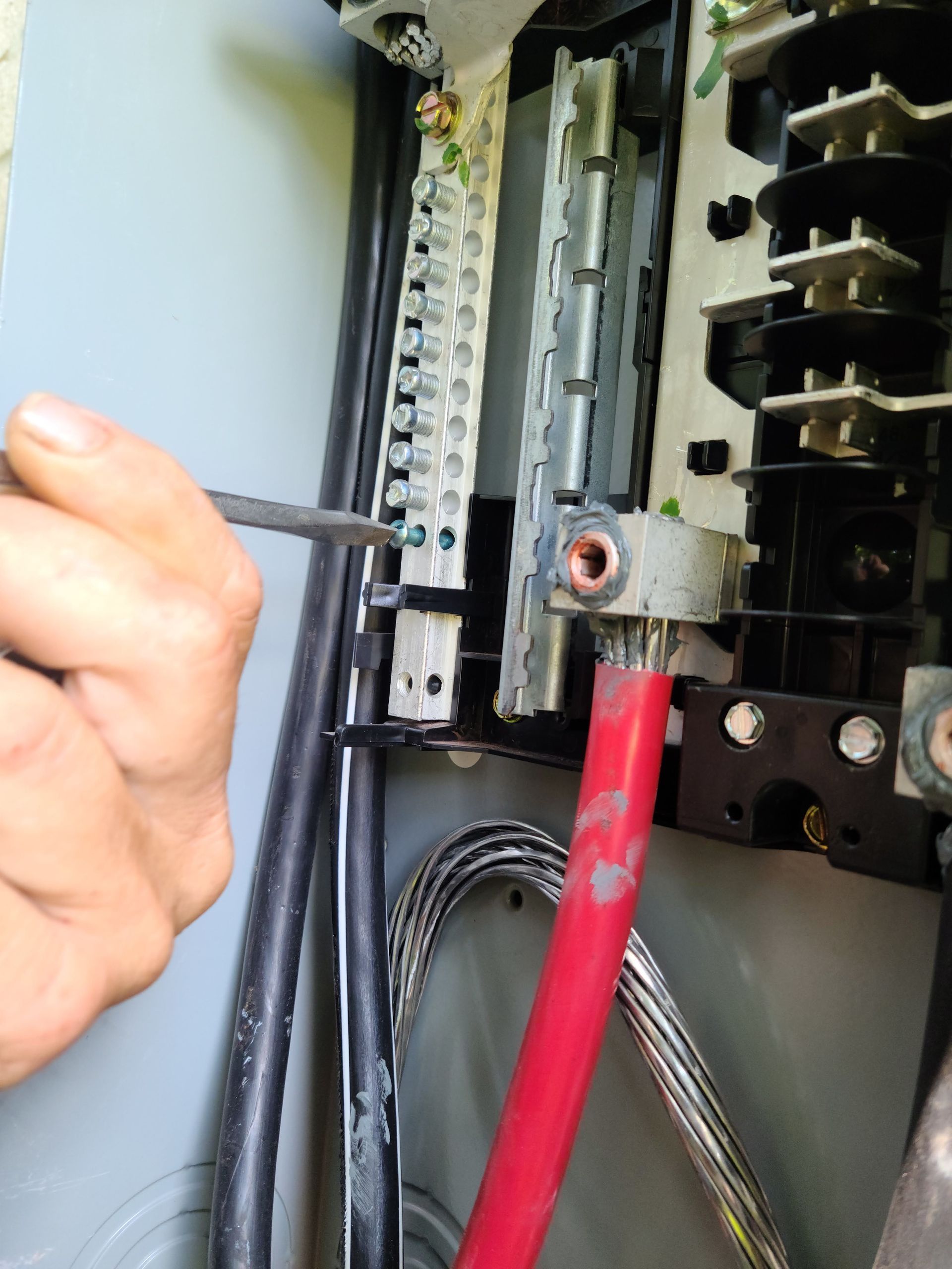 Person using a screwdriver to tighten a screw in an electrical panel. Red wire visible.