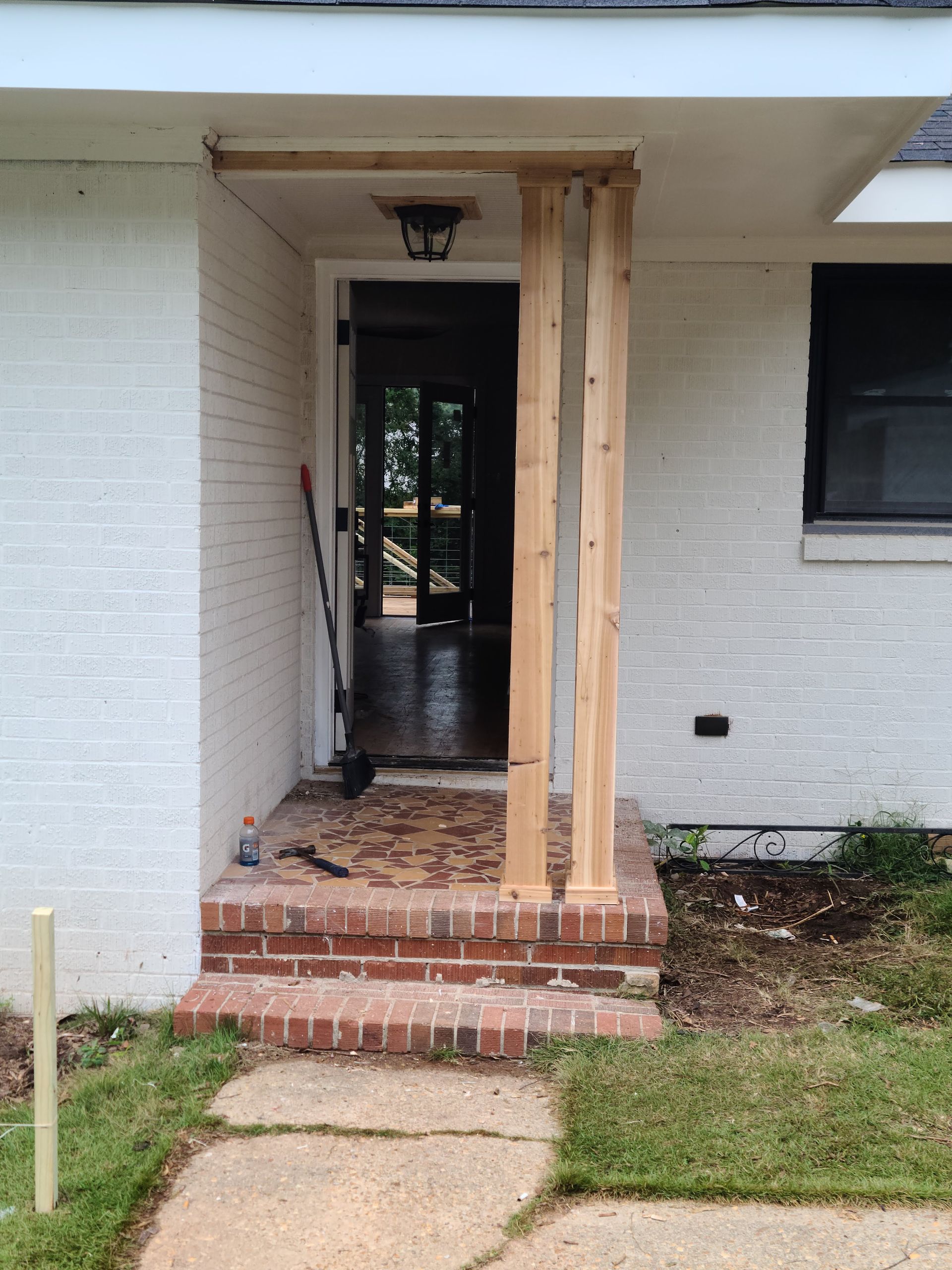 Entryway with brick steps, white brick walls, and new wooden support posts.