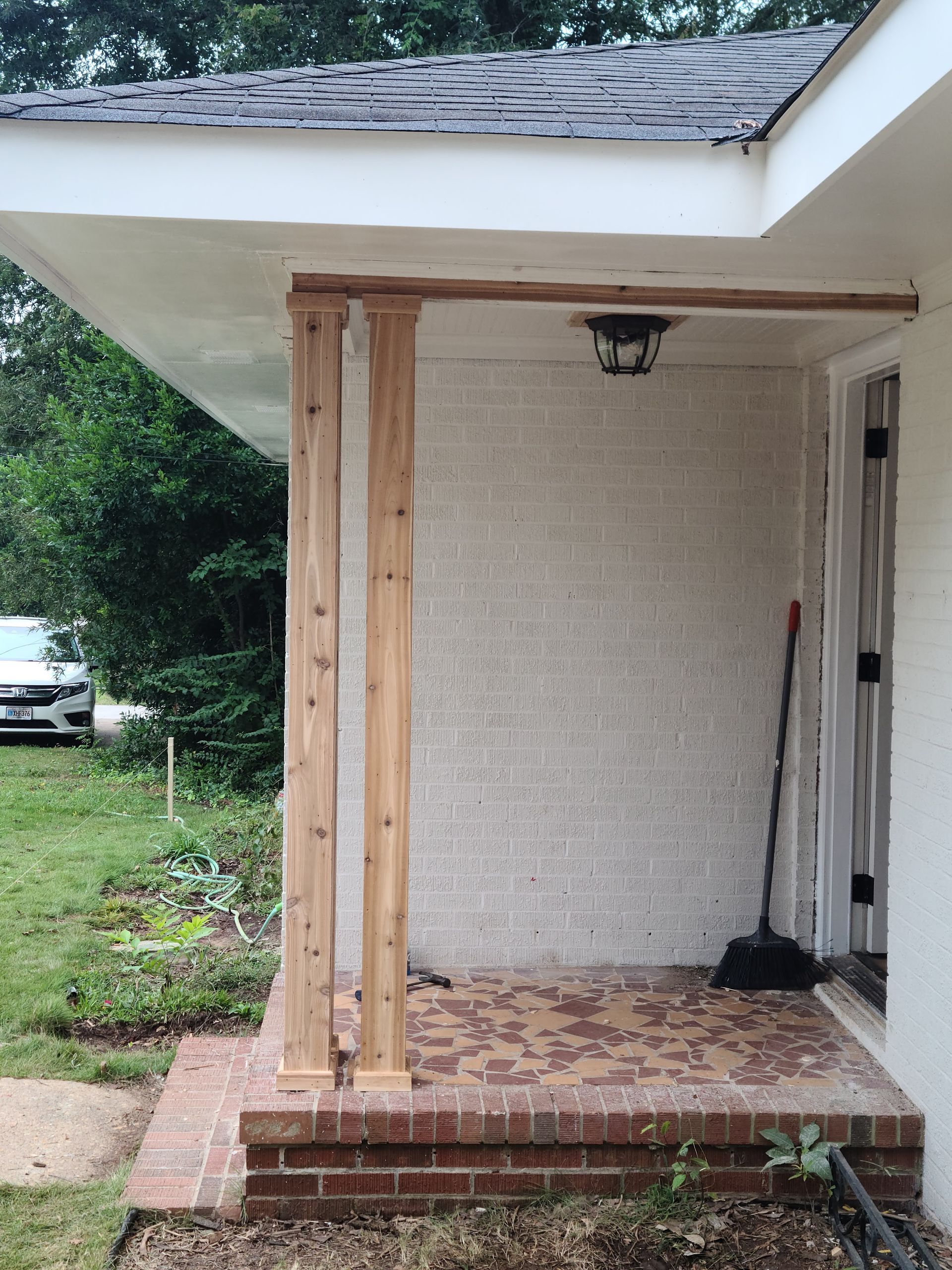 Front porch with brick steps, two wooden pillars, and a white stucco wall.