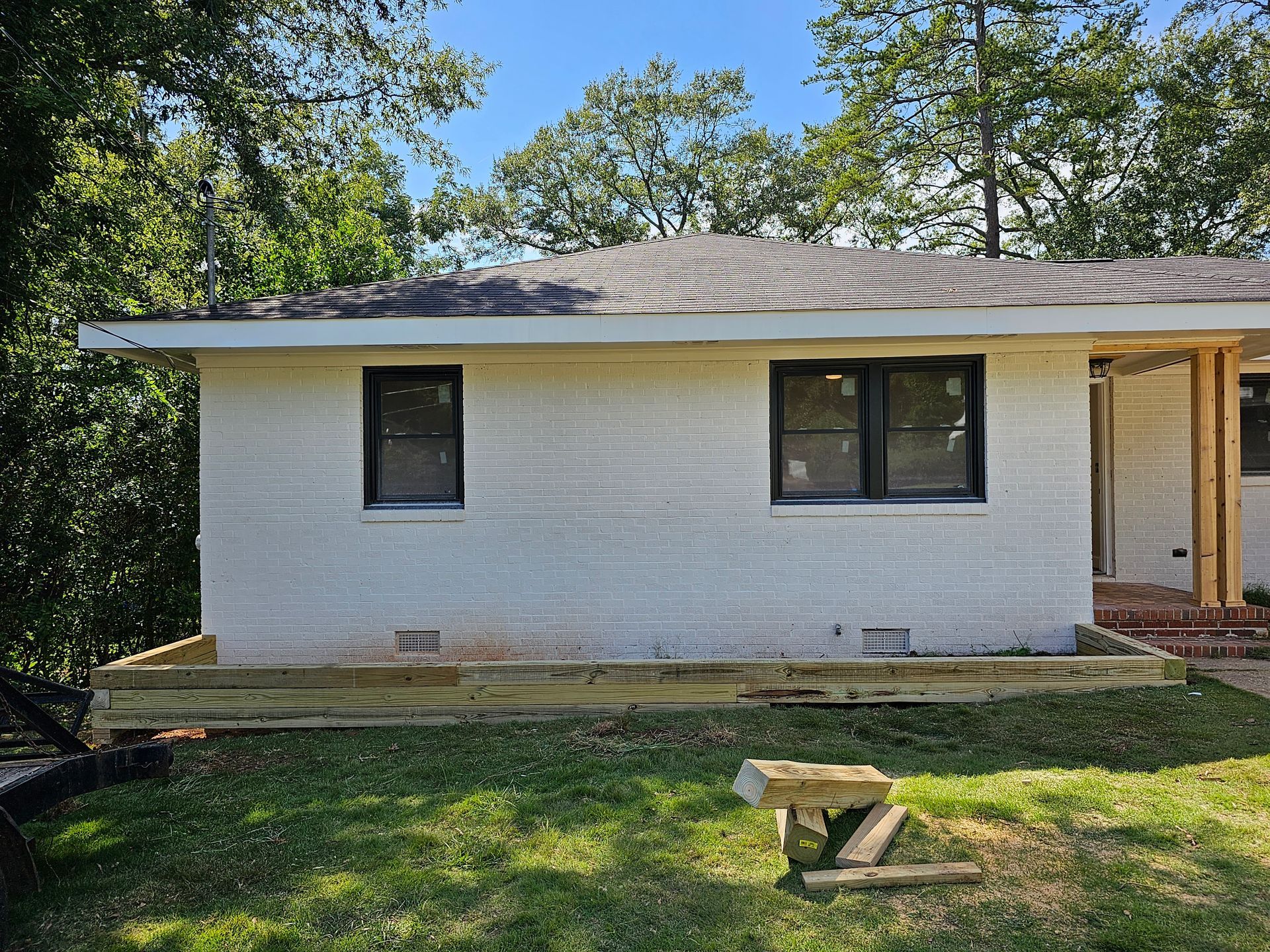 White brick house with black windows, wooden trim, and a green lawn under a blue sky.