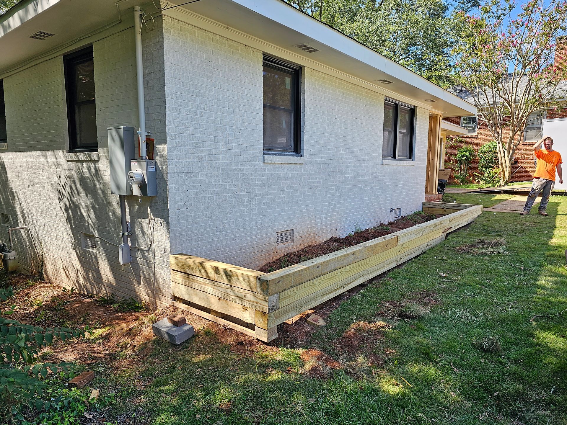 Wooden planter box built along a house wall, person standing nearby on grass.