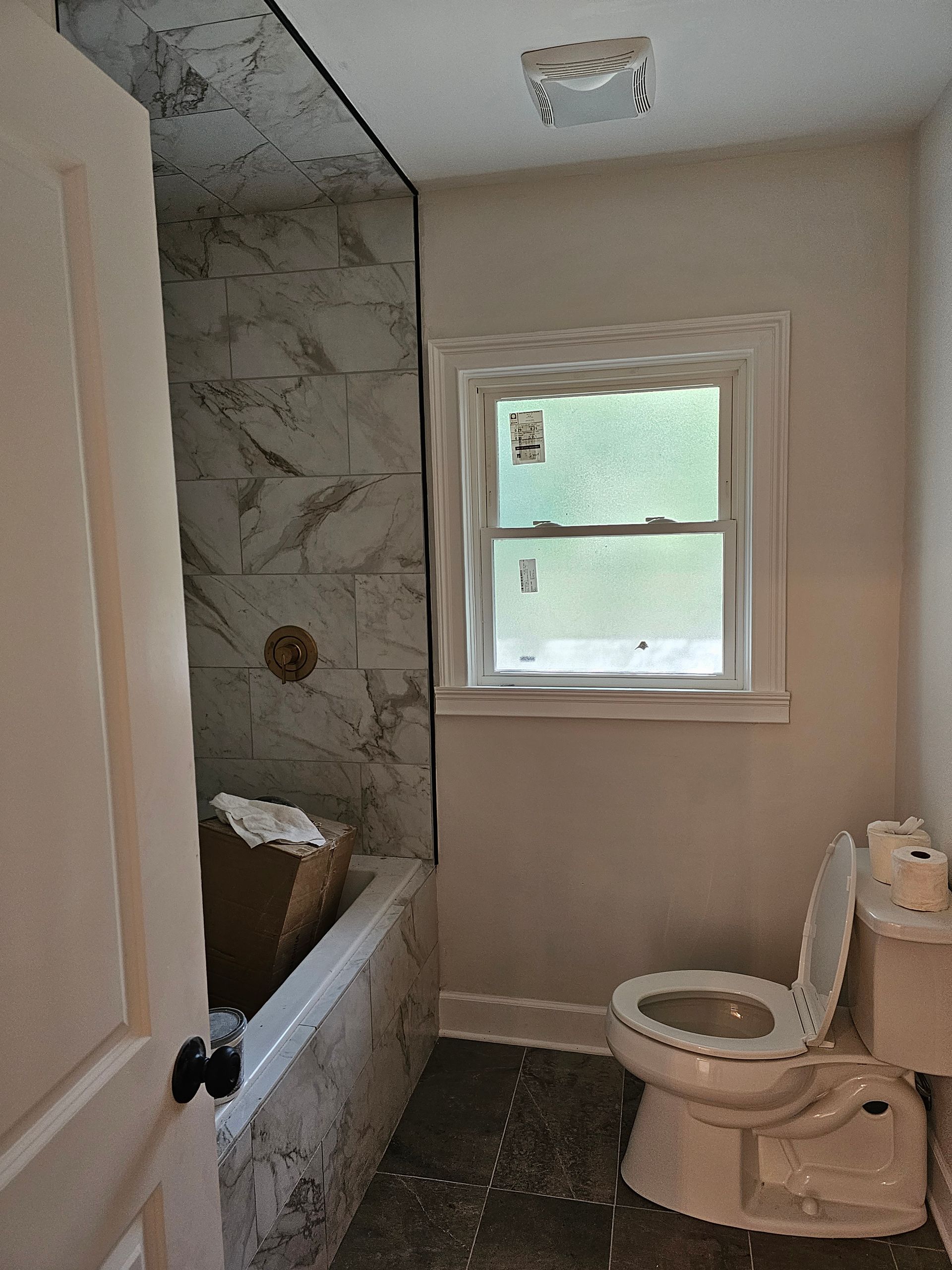 Bathroom with partially tiled shower/tub, window, and toilet; interior view.