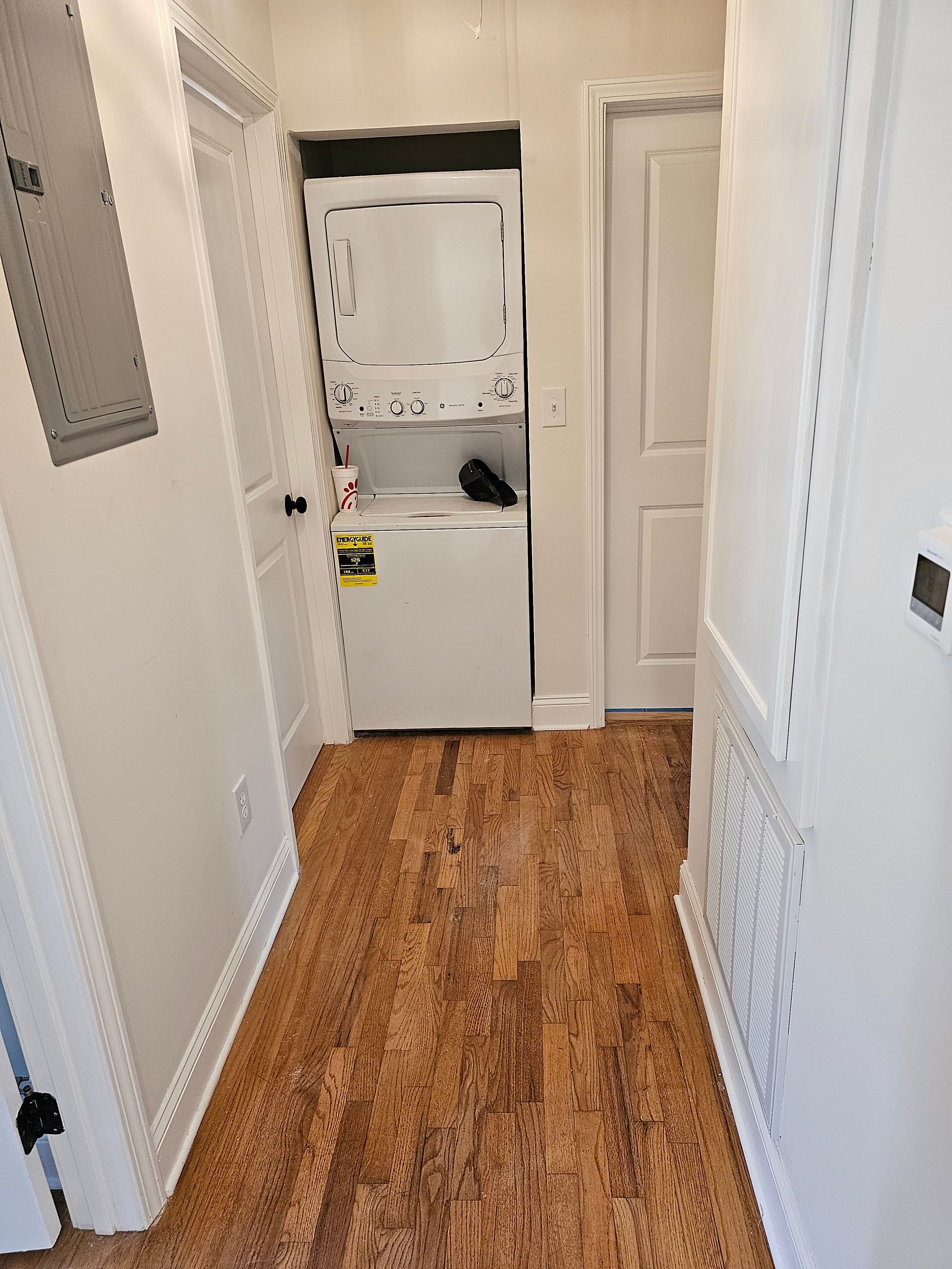 Hallway with white walls, wood floor, stacked washer/dryer, and two doors.