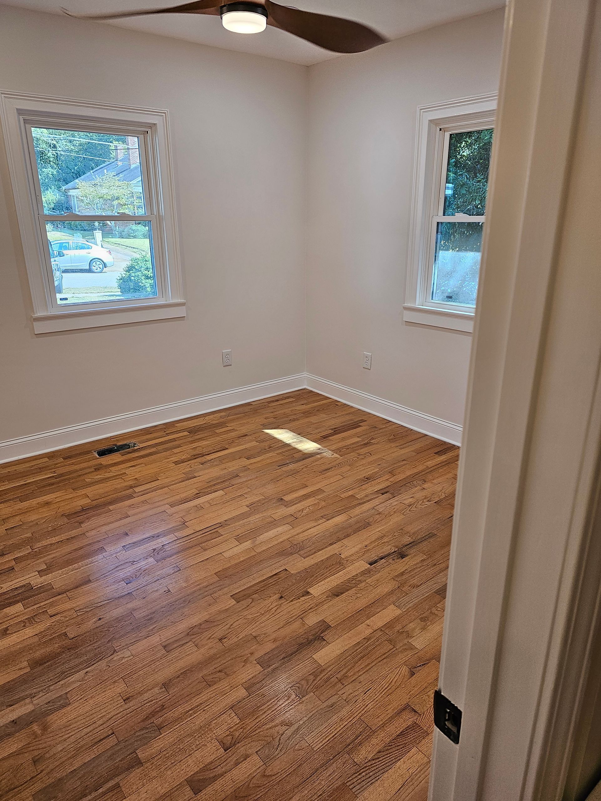 Empty room with wood floor, two windows, and a ceiling fan.