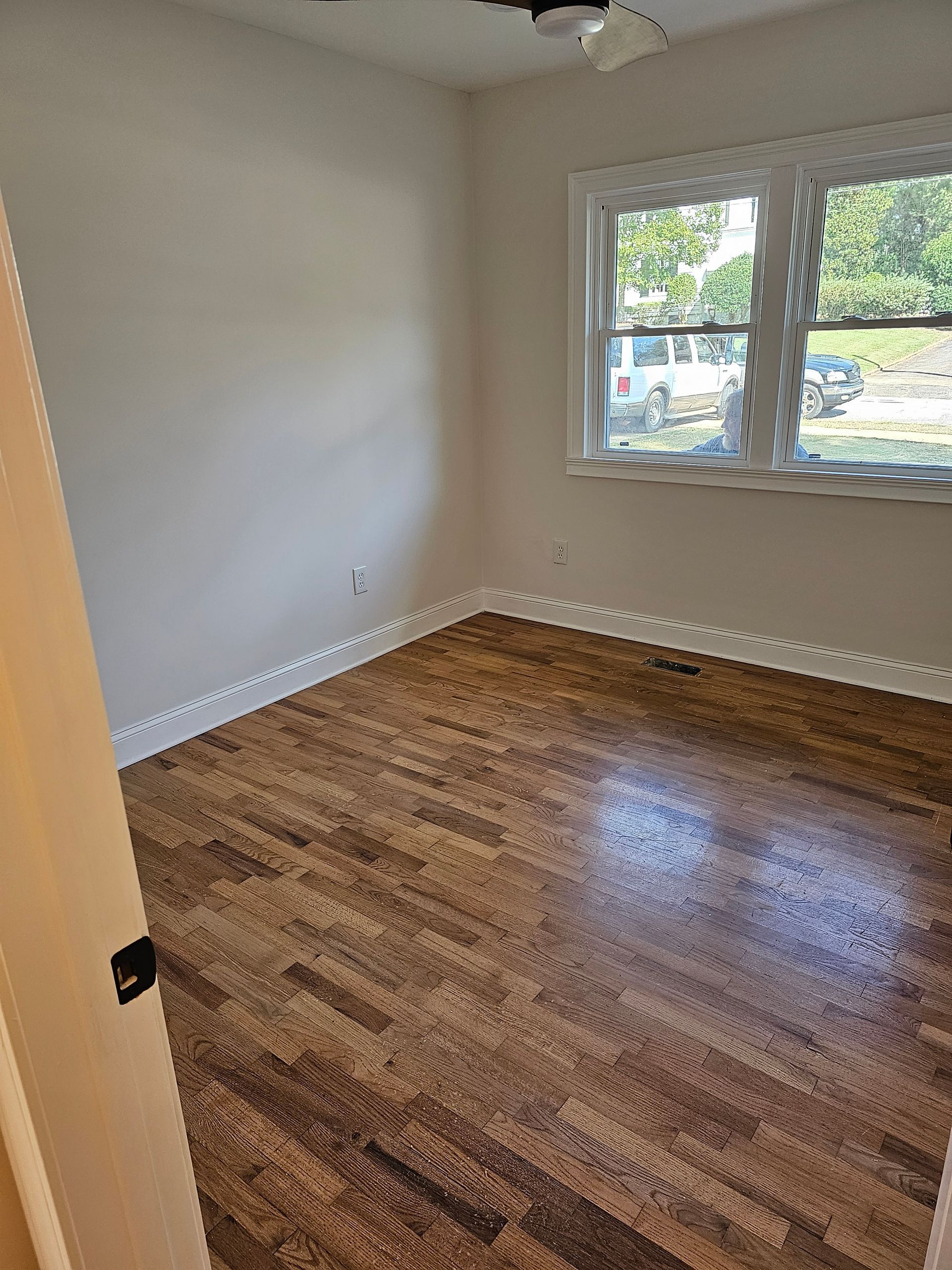 Empty room with hardwood floors, white walls, window, and a door opening.