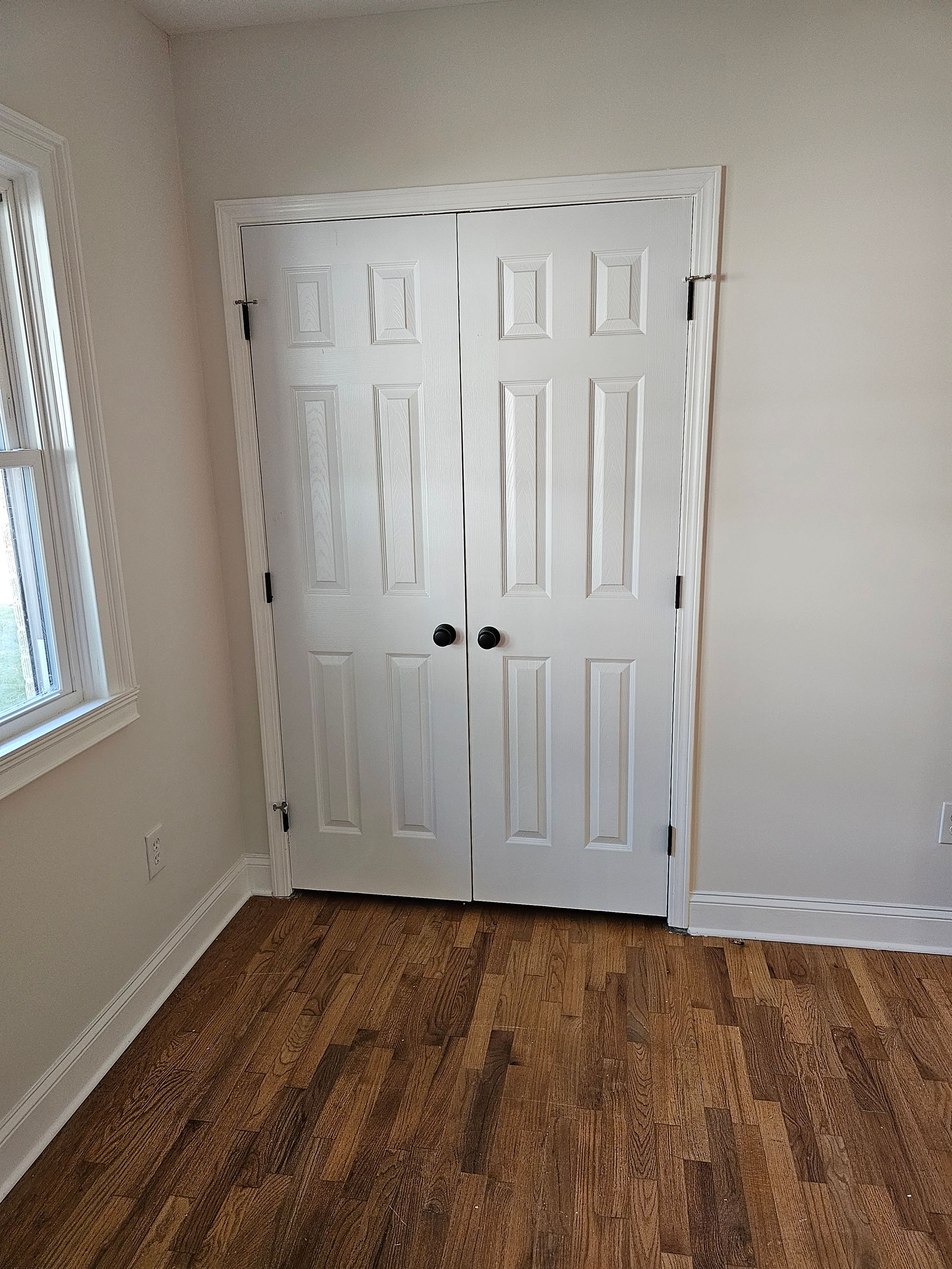 White double doors framed in a room with wood-look flooring and a window.
