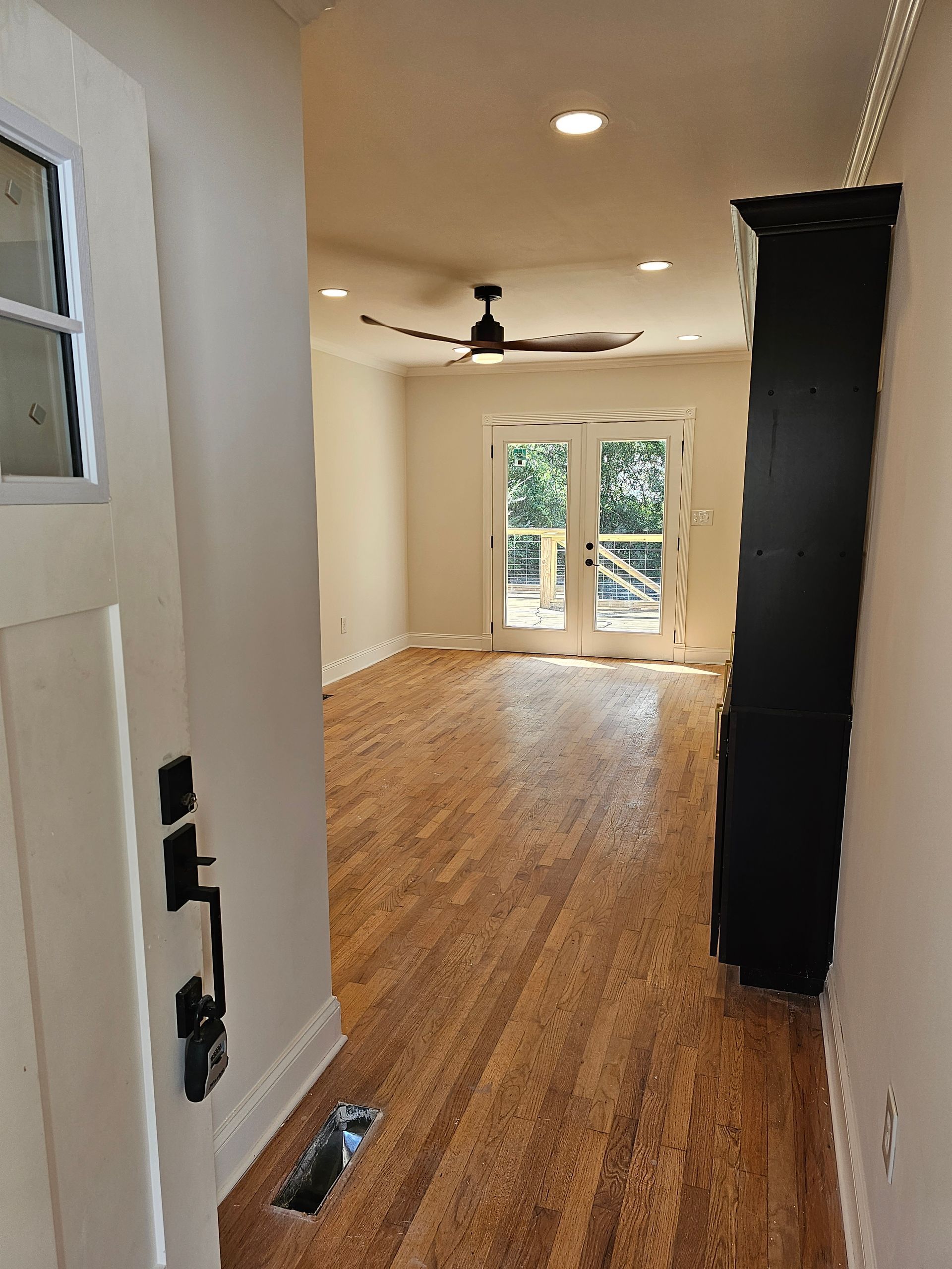 View from a doorway into a sunlit room with hardwood floors, a ceiling fan, and French doors leading to a deck.