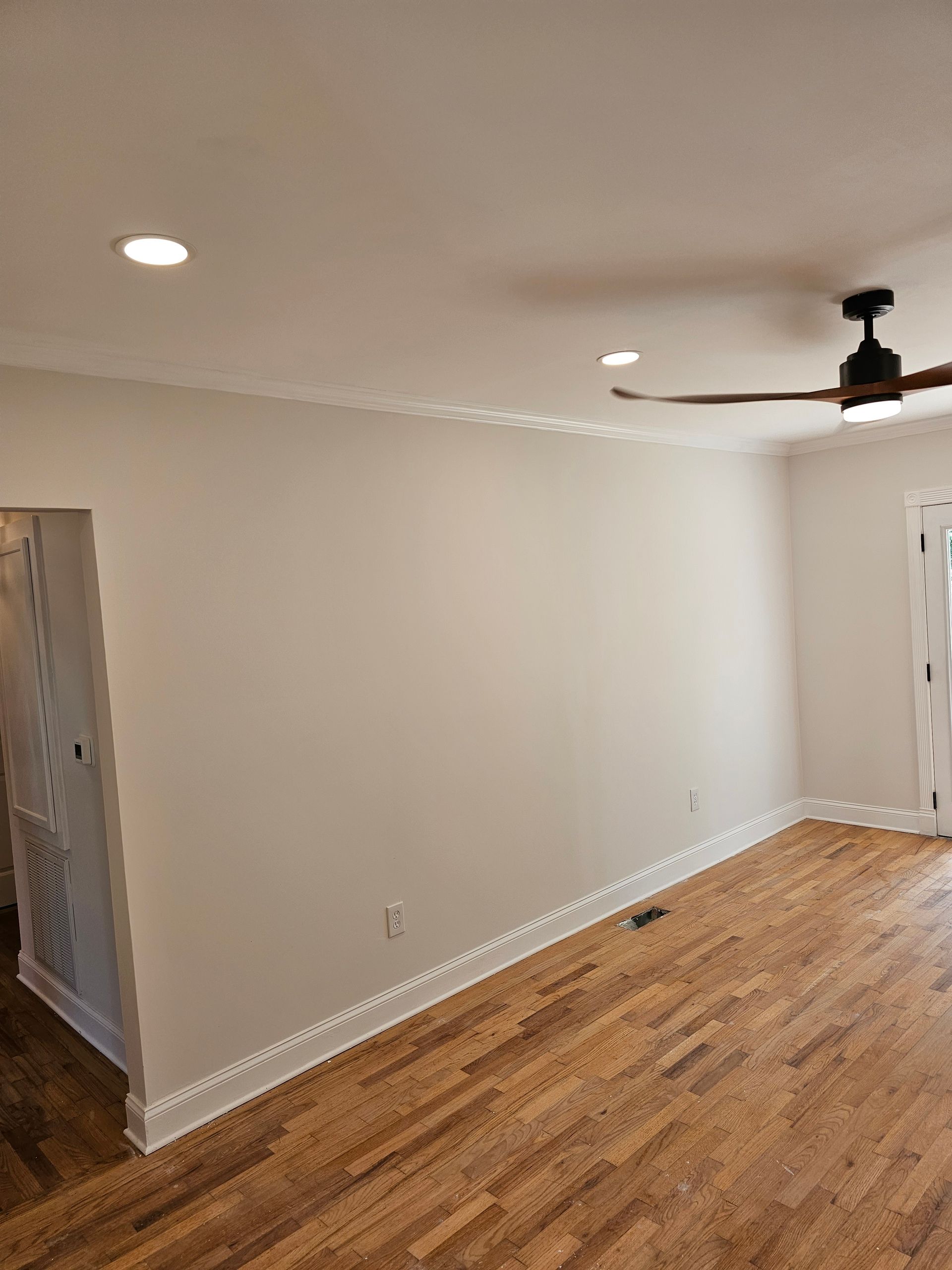 Interior view of a room with hardwood floors, white walls, and a ceiling fan.